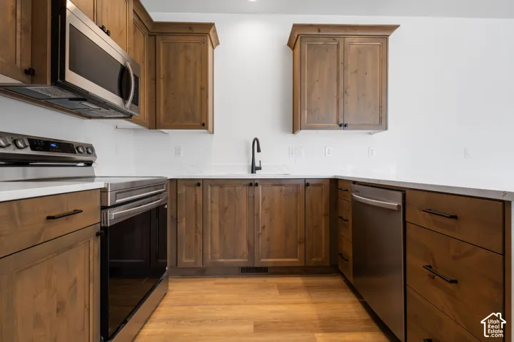 Contemporary kitchen featuring wood-finish cabinetry, stainless steel appliances, white countertops, and a matte black faucet