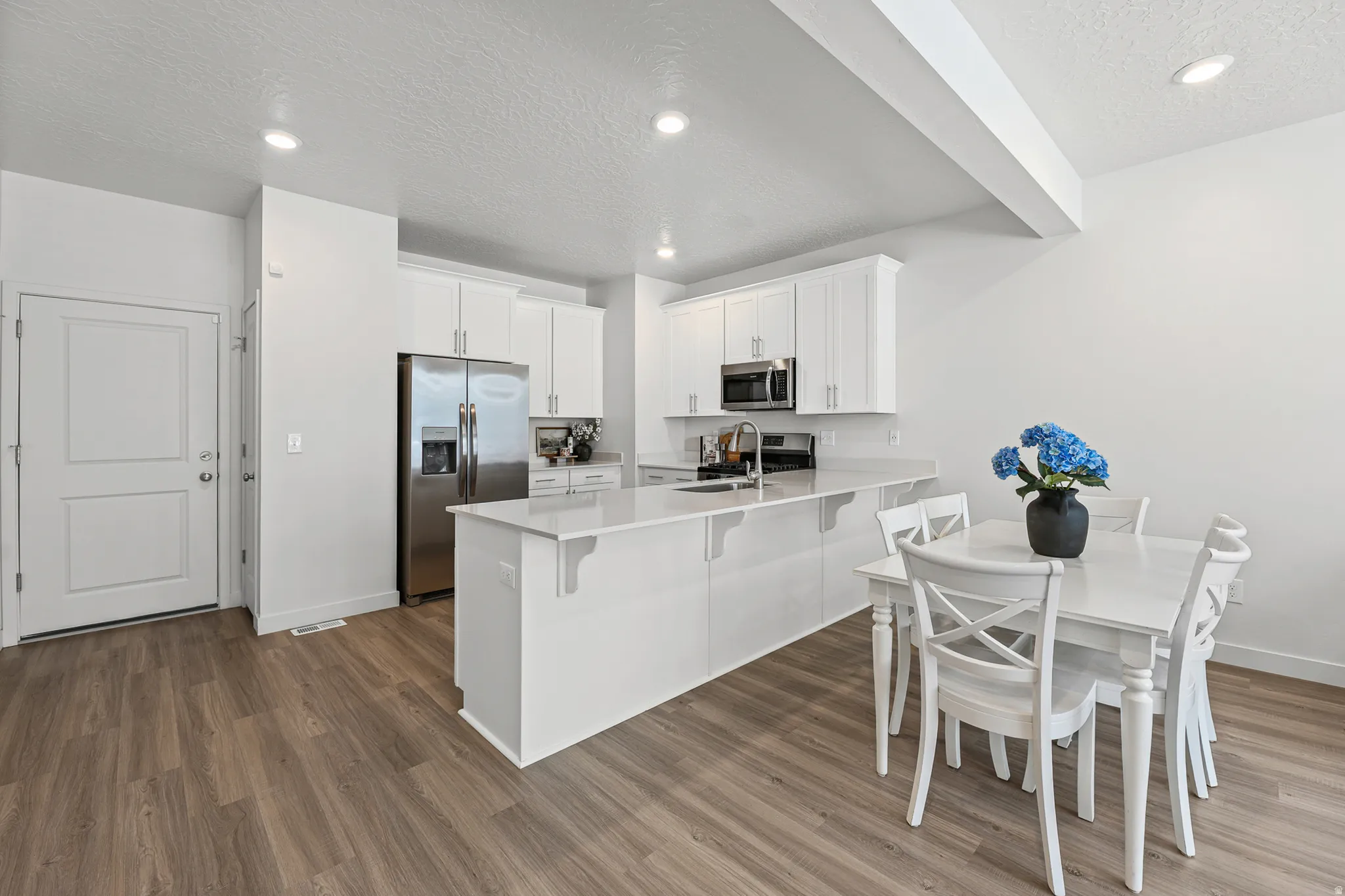 Open-concept kitchen and dining area featuring wood-finish flooring, white cabinetry, stainless steel appliances, and recessed lighting