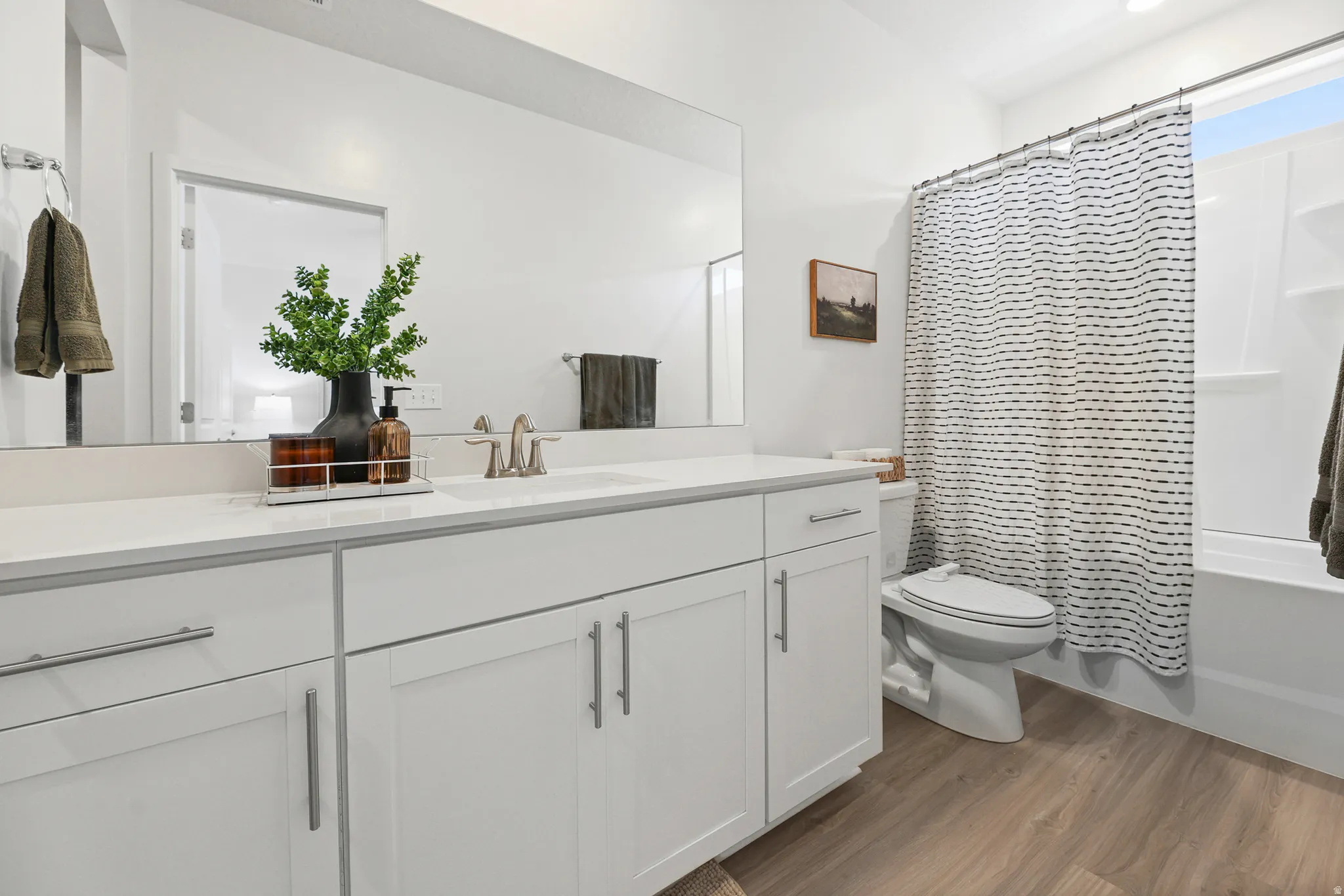 White shaker vanity cabinetry with brushed nickel hardware, expansive countertop, large mirror, and a tub/shower combination with a white surround