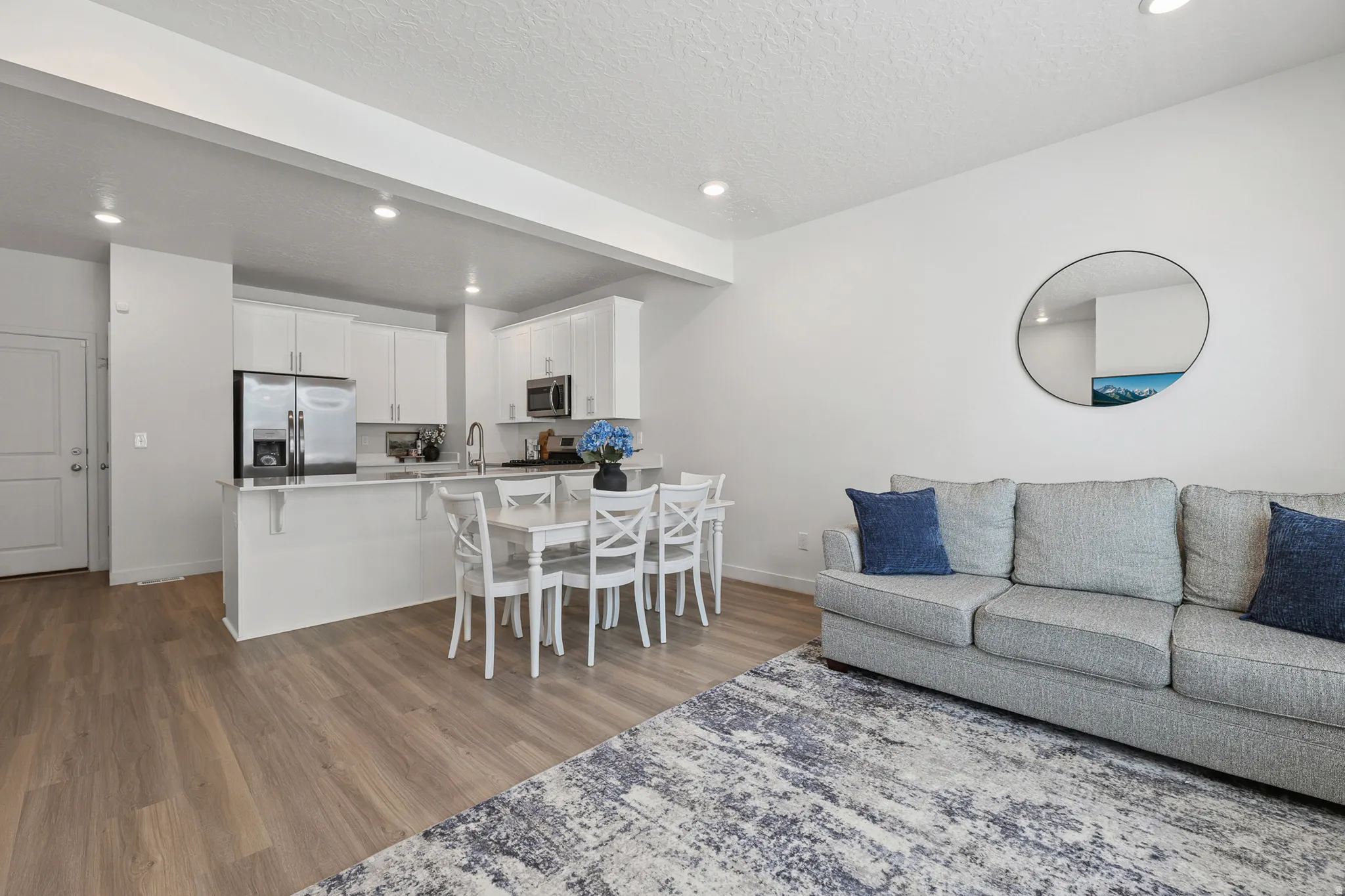 Open-concept living area featuring wood-finish flooring, white cabinetry, stainless steel appliances, and recessed lighting