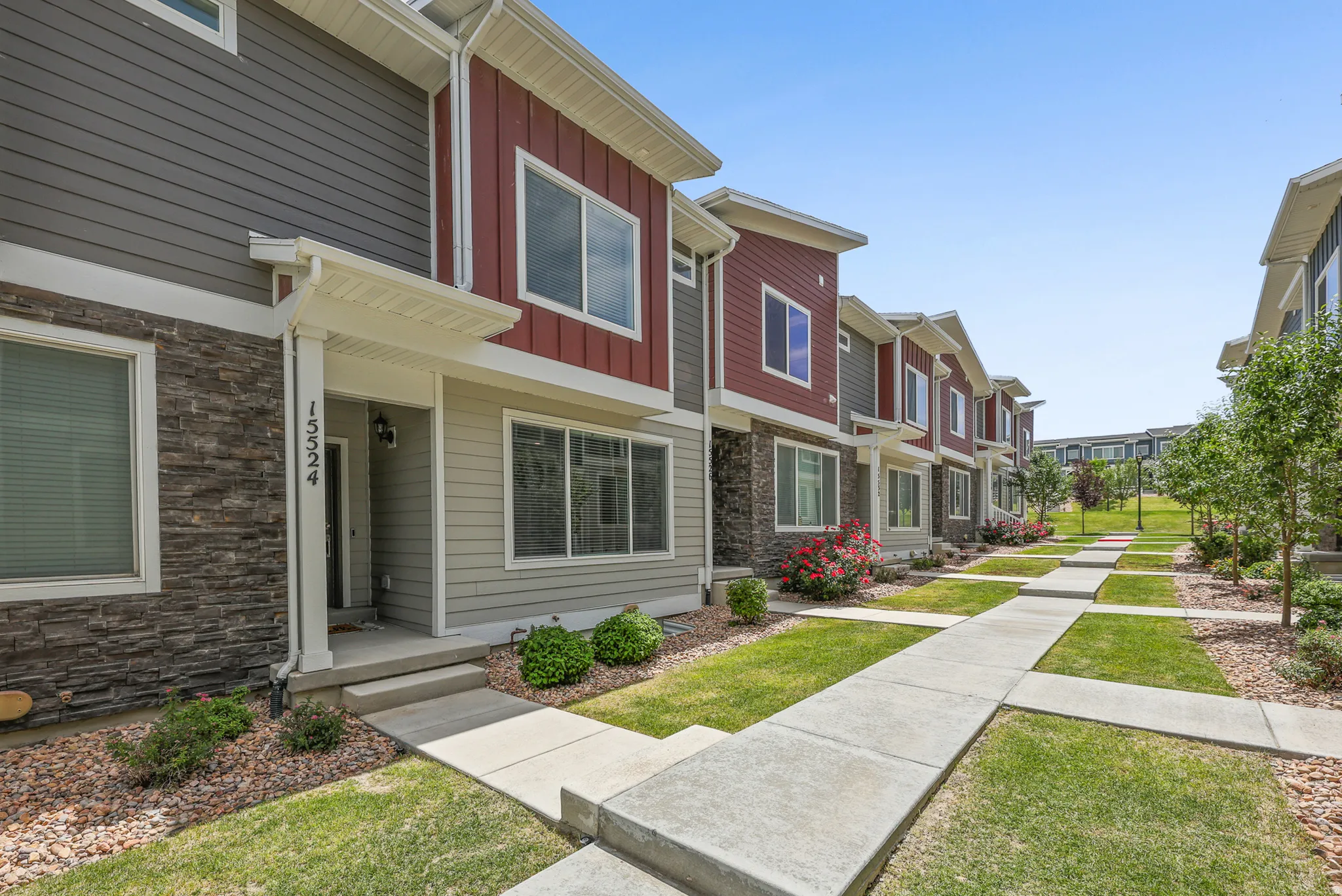 Contemporary townhouse exterior featuring a covered entry, stone veneer accents, horizontal siding, and a concrete walkway