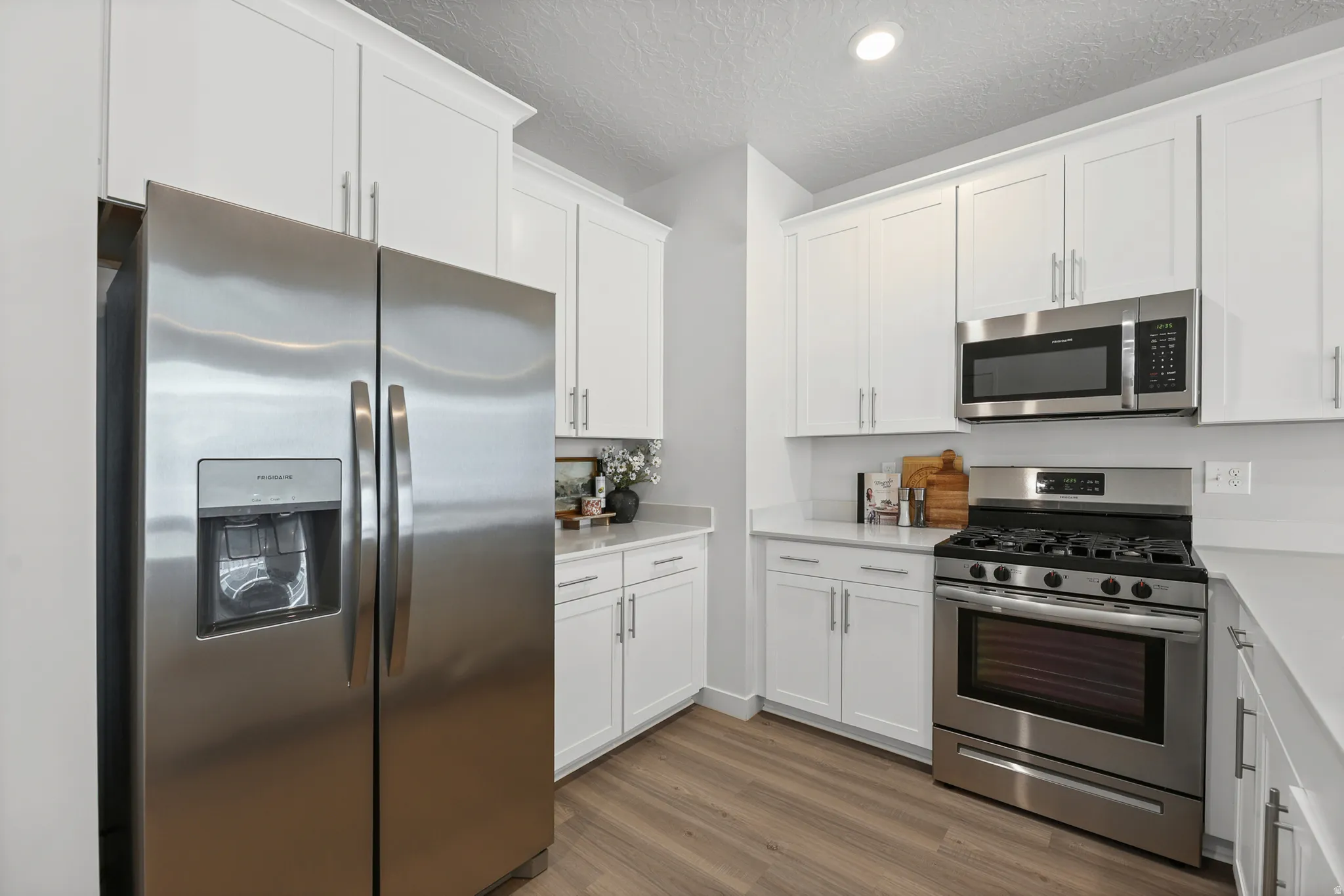 Kitchen featuring stainless steel appliances, white cabinetry, light countertops, a built-in microwave, and wood-finish flooring