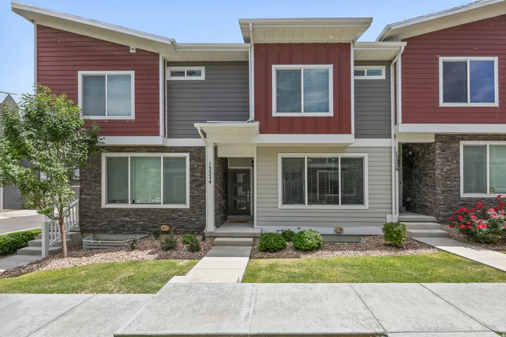 Modern multi-level exterior featuring red and gray siding, stone accents, white window frames, and a concrete walkway
