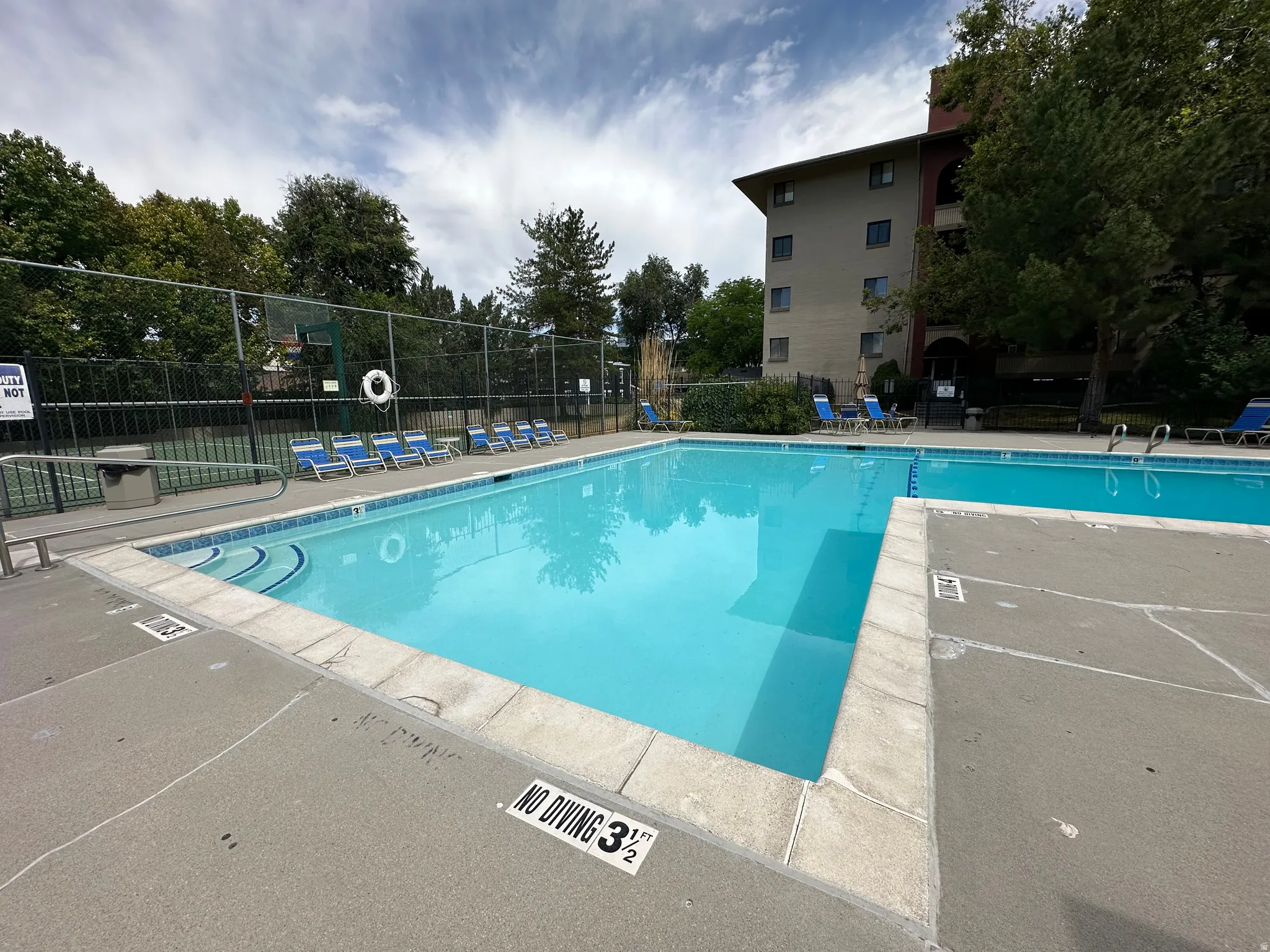 Main swimming pool featuring a shallow area with steps, bordered by concrete decking and lounge chairs