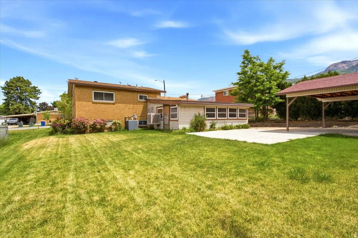 Expansive lawn area featuring a paved patio and a covered carport with a red roof