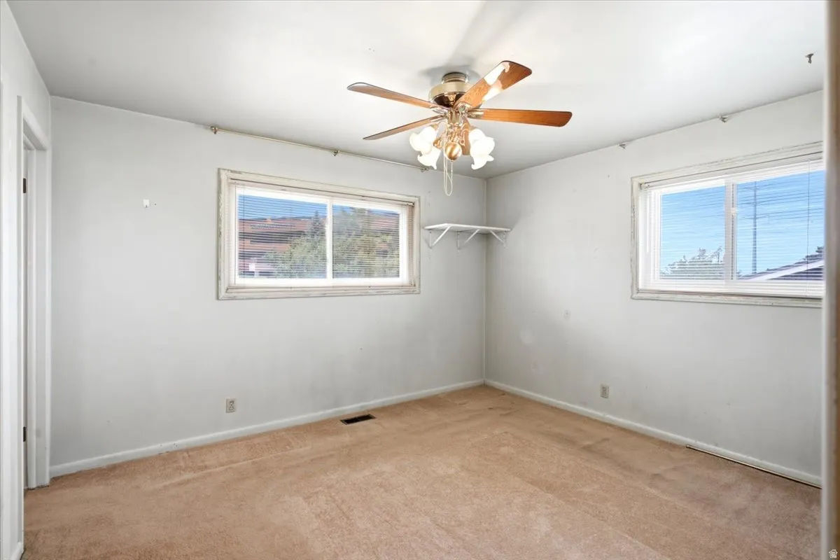 Room with ceiling fan light fixture, two windows with blinds, and wall-to-wall carpeting