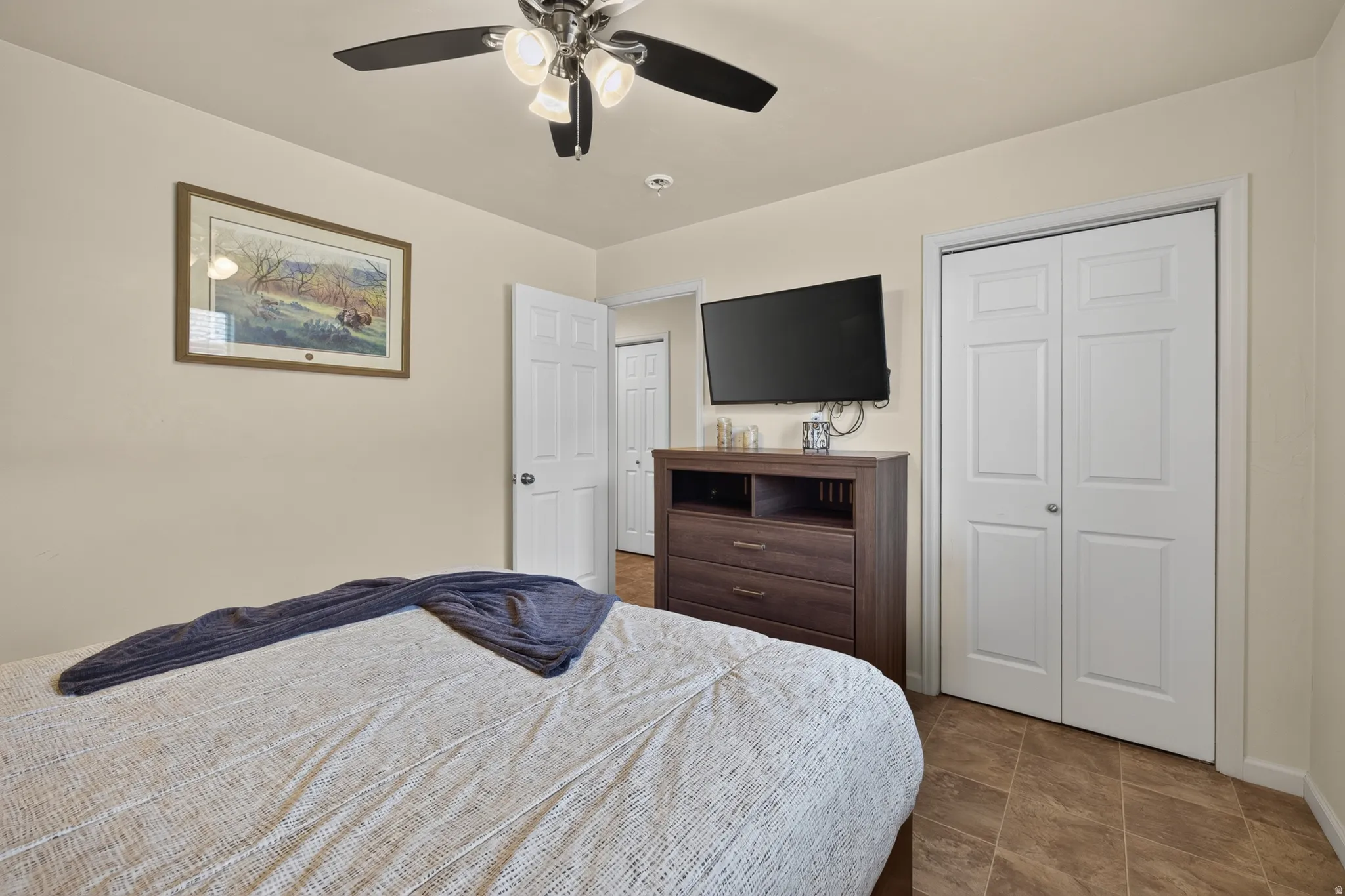 Bedroom with durable tile flooring, a ceiling fan with integrated lighting, and white bi-fold closet doors