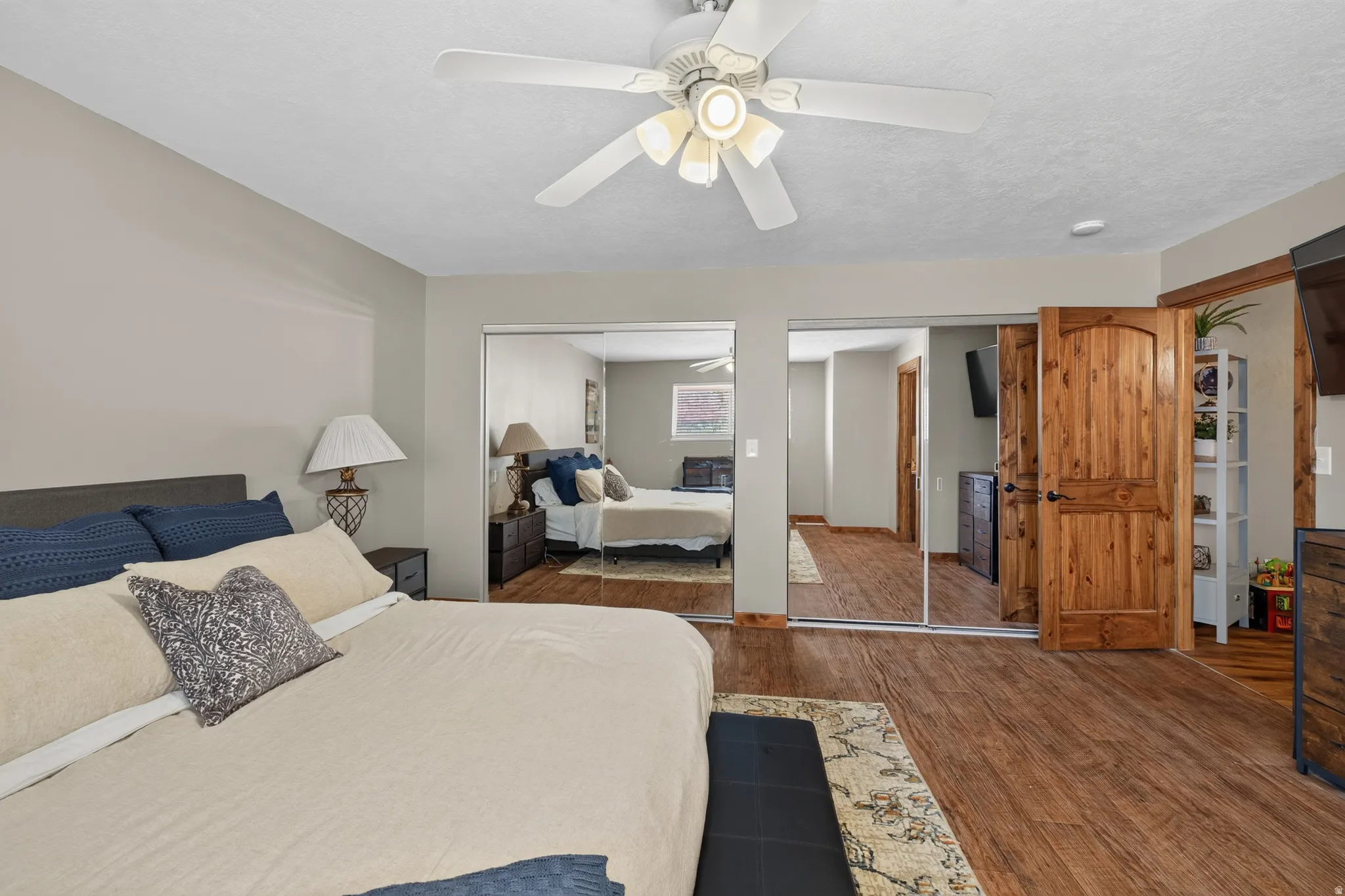 Bedroom with wood-finish flooring, light grey painted walls, and a ceiling fan with integrated lighting