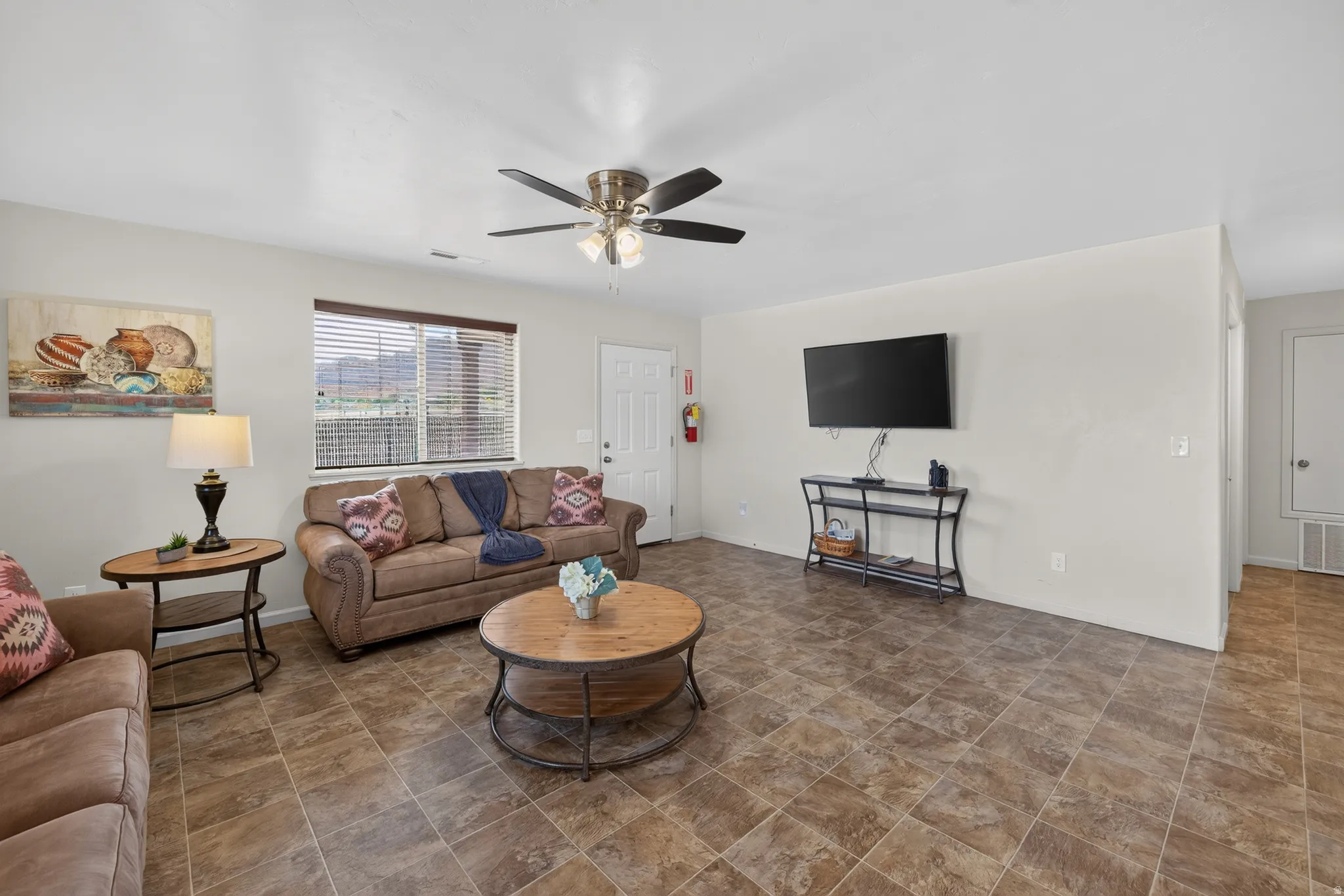 Spacious living area featuring tiled flooring, a ceiling fan, and a window with horizontal blinds