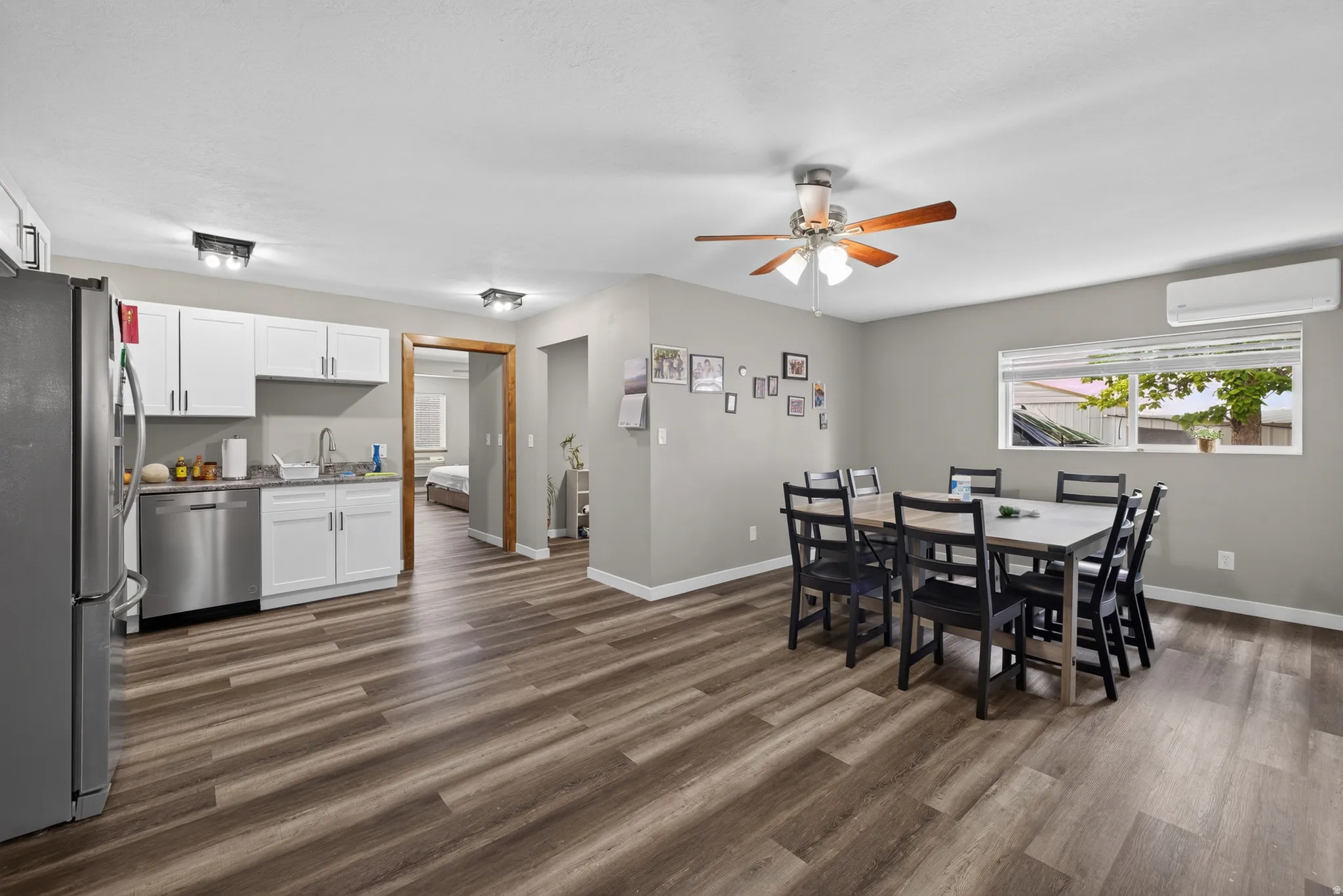 Open-concept living area featuring wood-finish flooring, a ceiling fan with integrated lighting, and a window with blinds