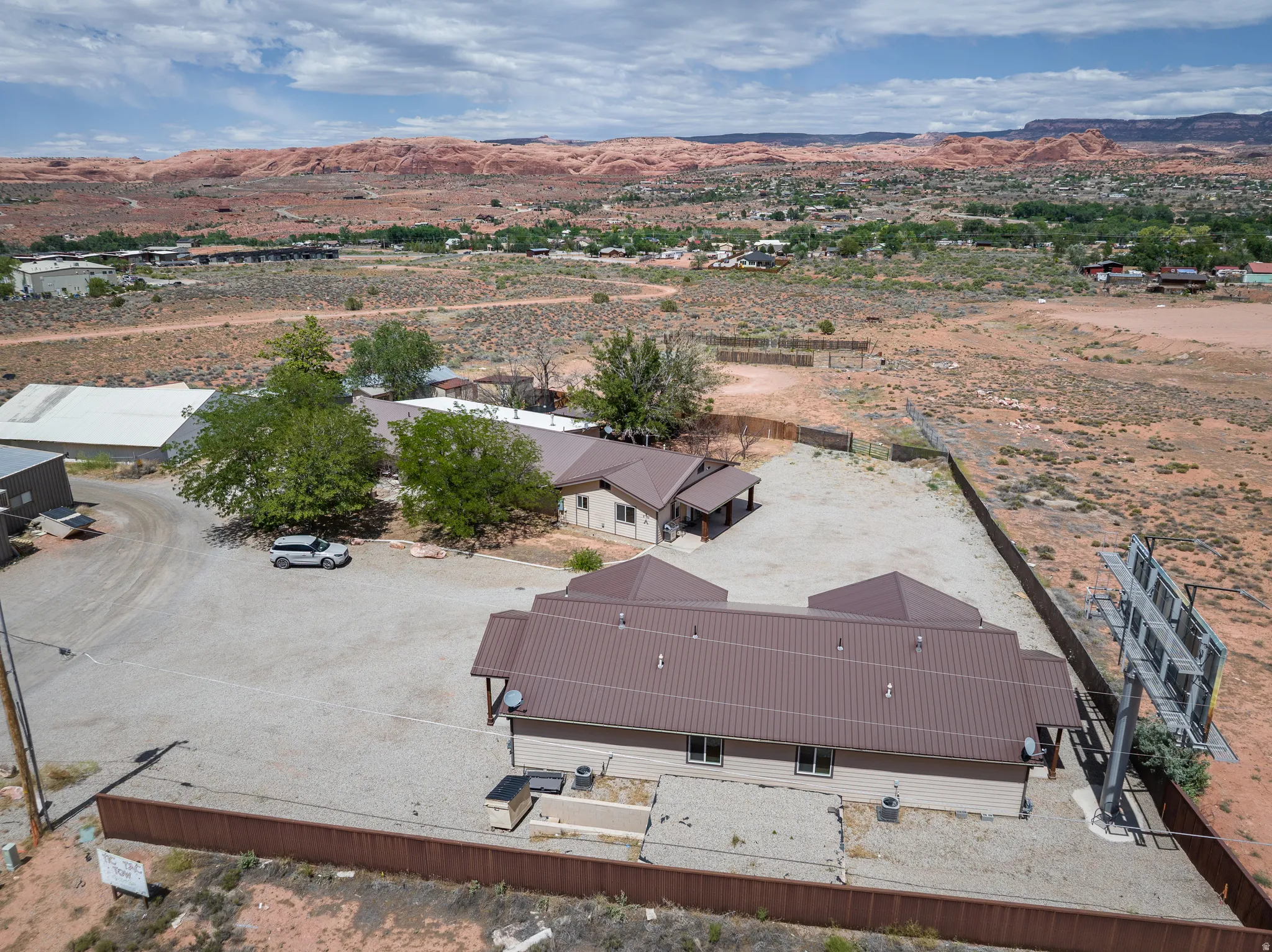 Aerial depiction of a property featuring two buildings with brown metal roofing, expansive gravel parking areas, and partial perimeter fencing