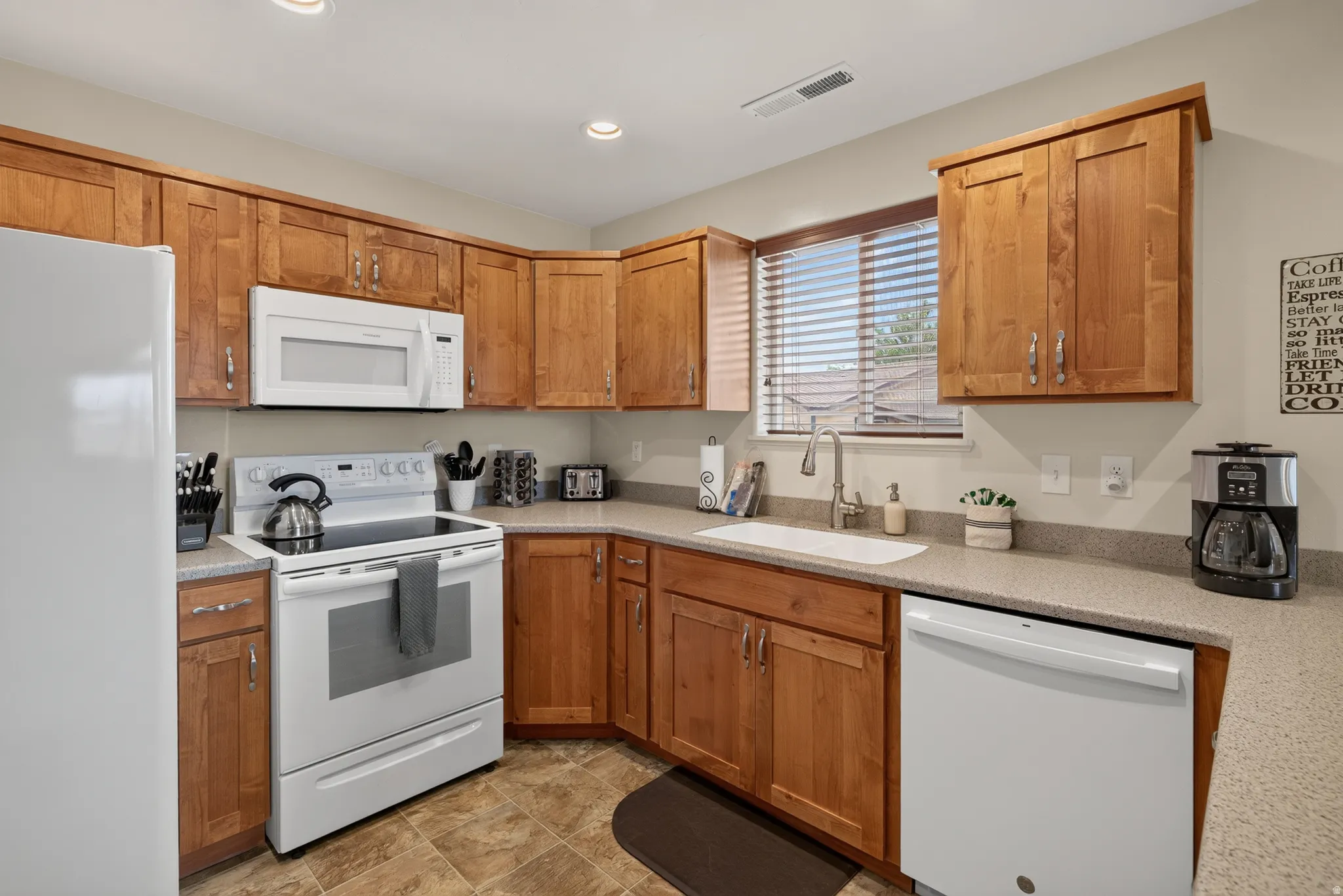 Kitchen featuring wood cabinetry, light-toned countertops, tile flooring, and white appliances including a refrigerator, range, microwave, and dishwasher