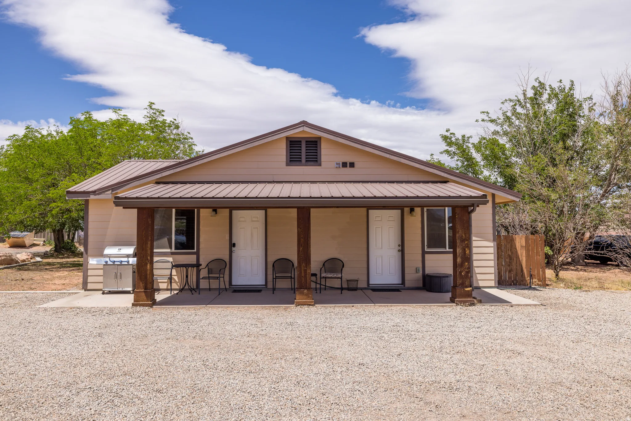 Exterior featuring a covered porch with exposed wood posts, tan siding, and a brown metal roof