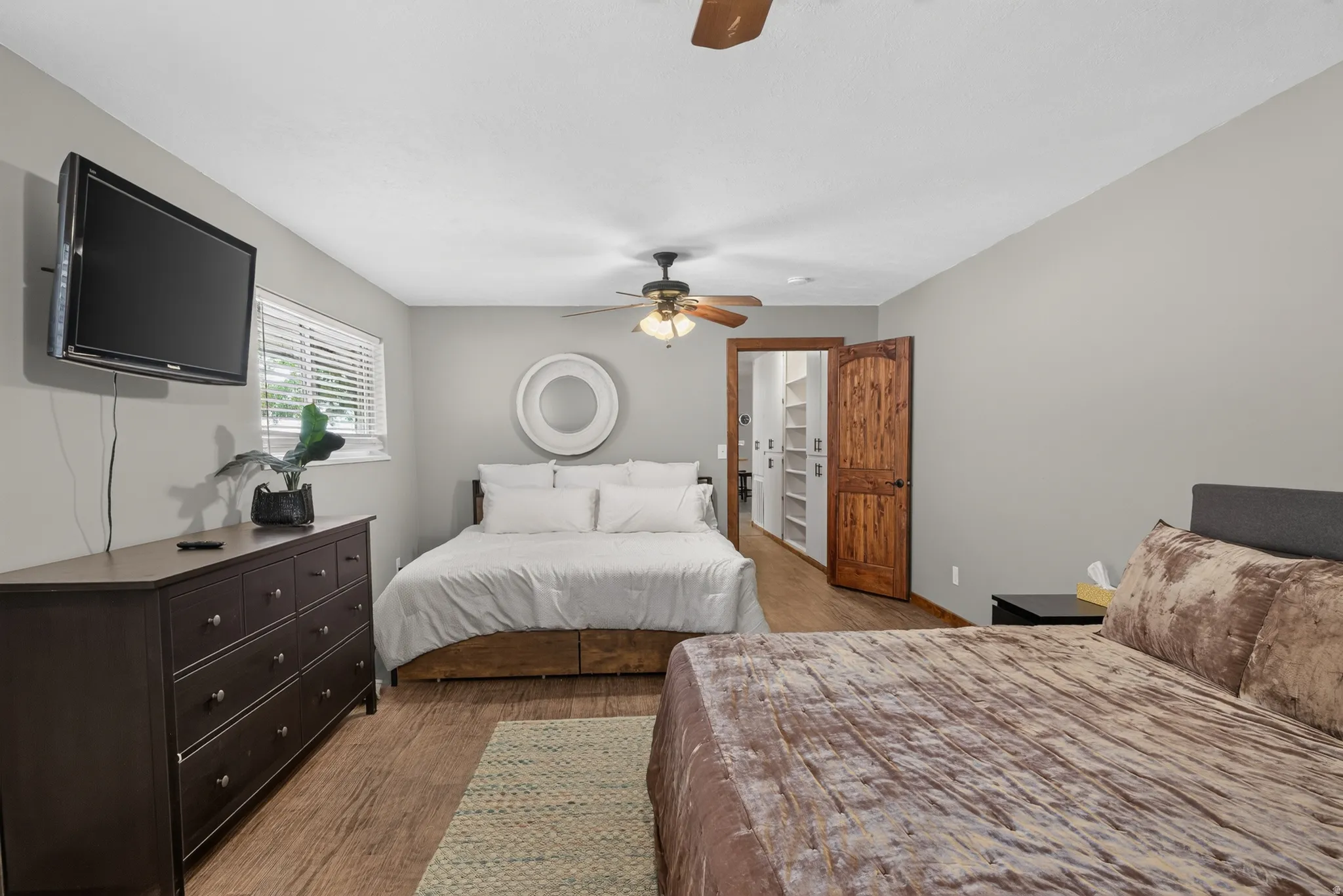 Bedroom featuring wood-finish flooring, a ceiling fan, window with blinds, and a closet with custom shelving and a wood door