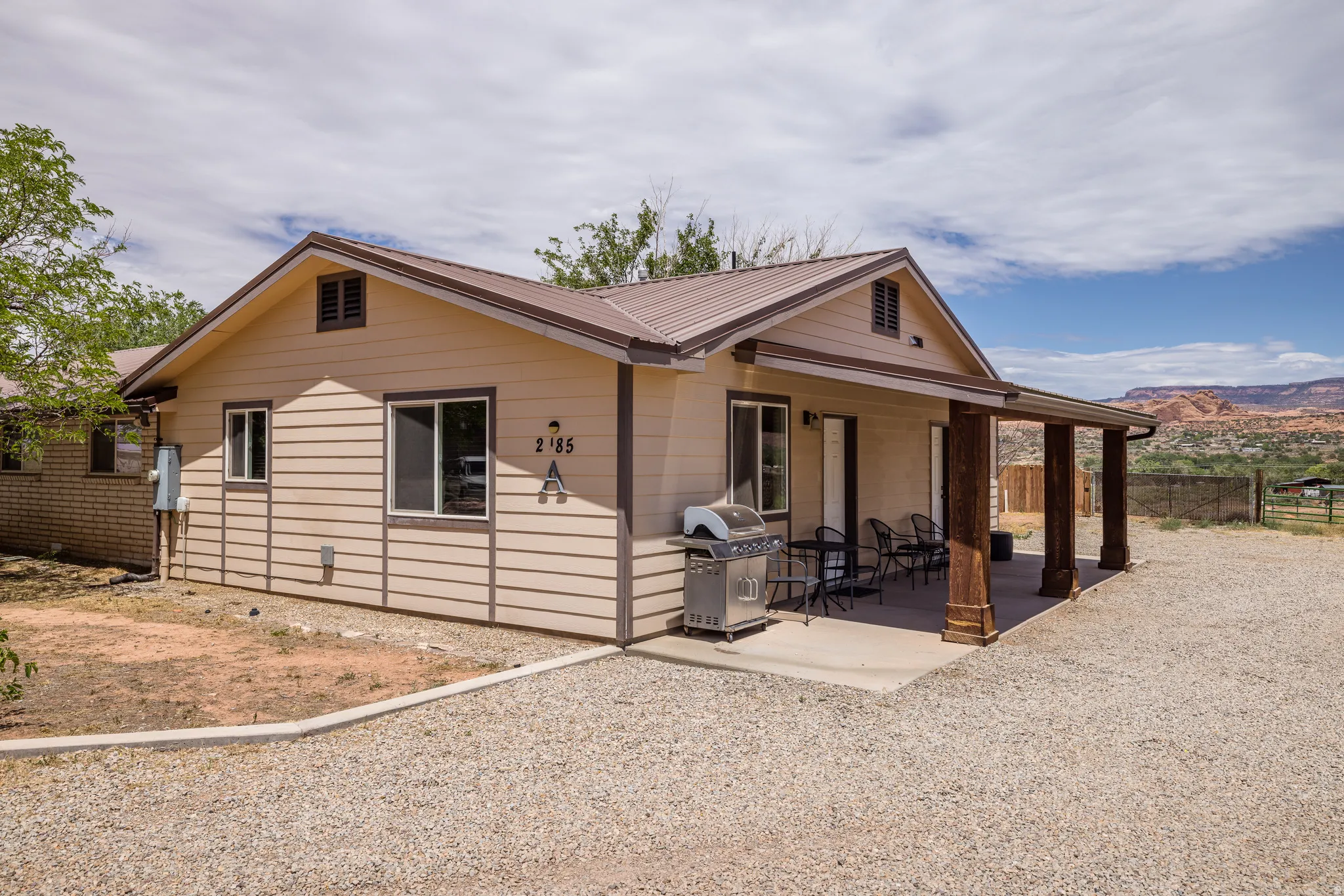 Exterior featuring light beige siding with dark trim, a brown metal roof, and a covered patio supported by decorative wood columns
