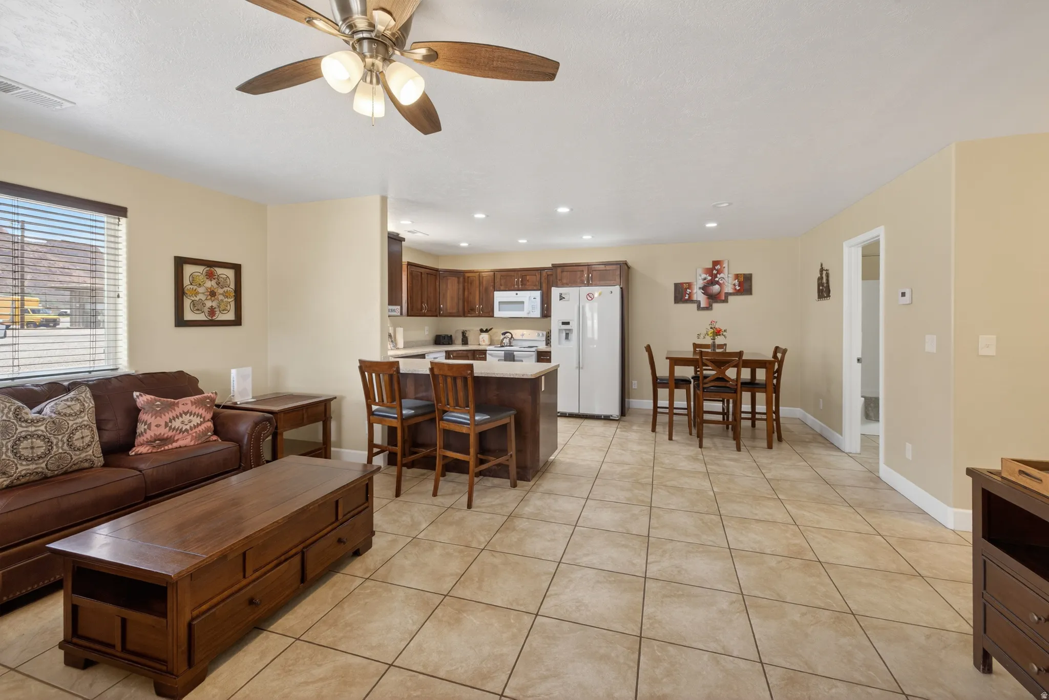 Open-concept living area featuring tile flooring, a ceiling fan, and a kitchen with dark wood-finish cabinetry, light countertops, and a breakfast bar