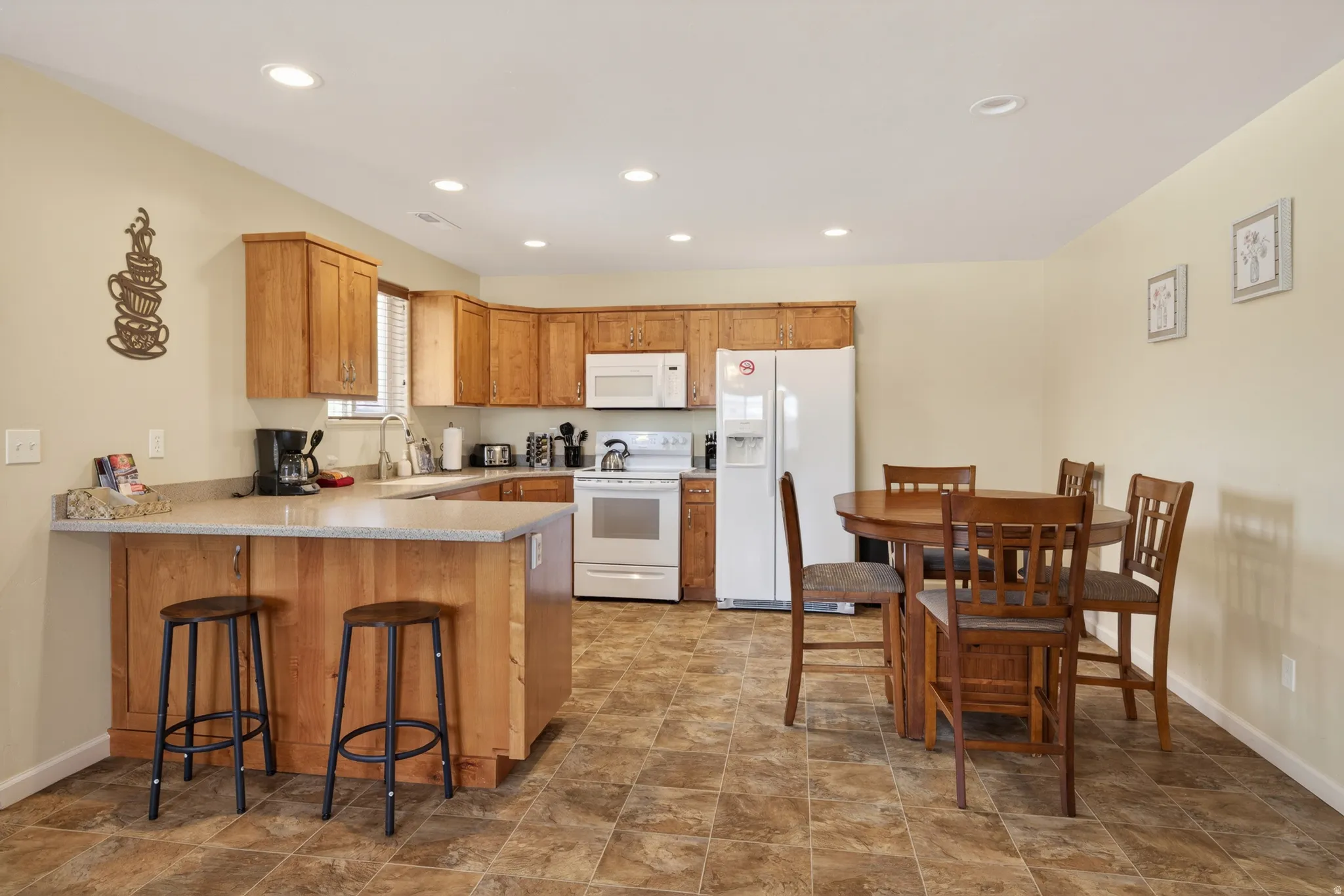 Open-concept kitchen featuring light-toned cabinetry, a breakfast bar with seating, white appliances, recessed lighting, and a tiled floor