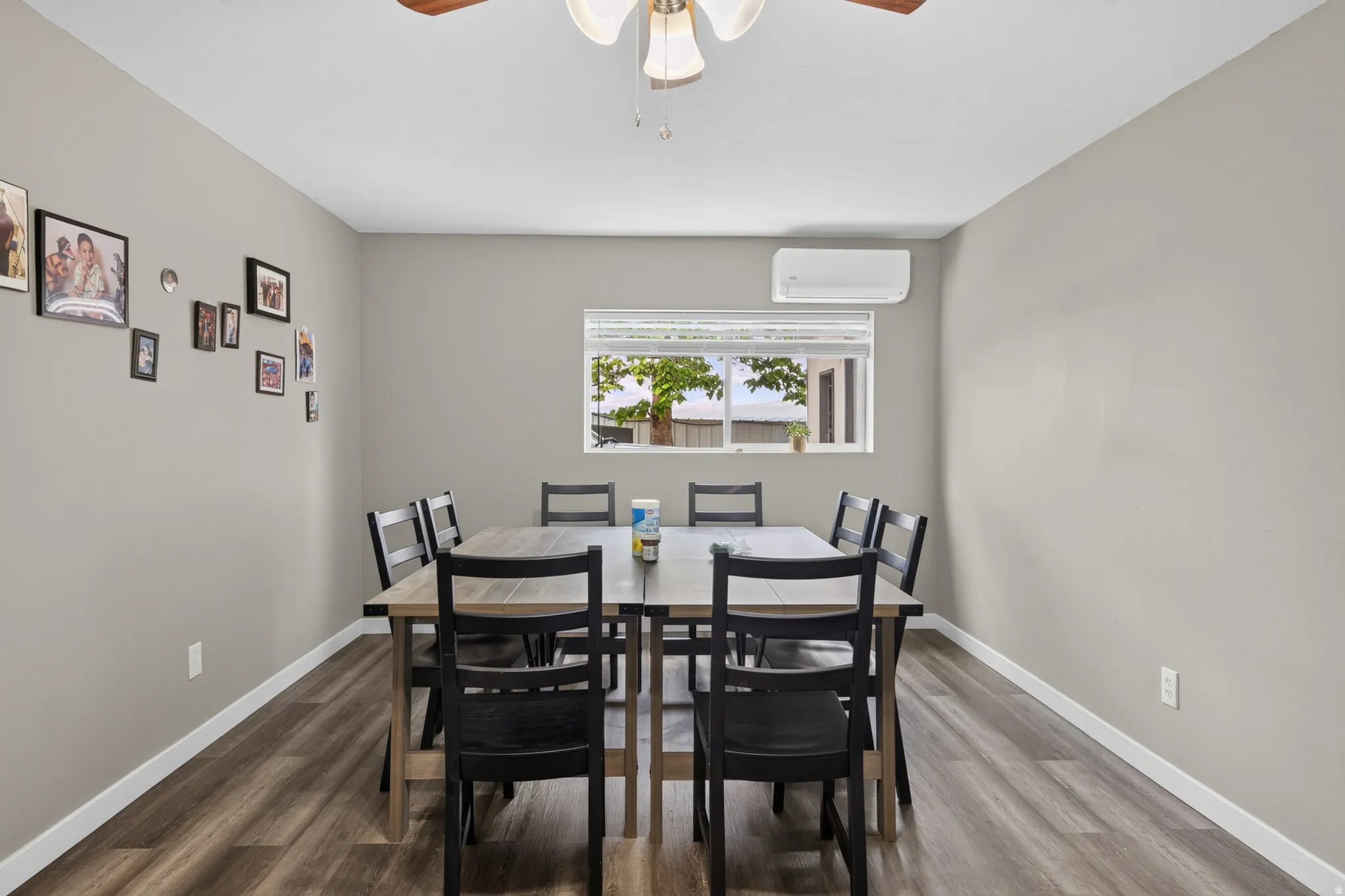 Spacious interior room featuring wood-finish flooring, light gray walls, a ceiling fan fixture, and a window with white blinds