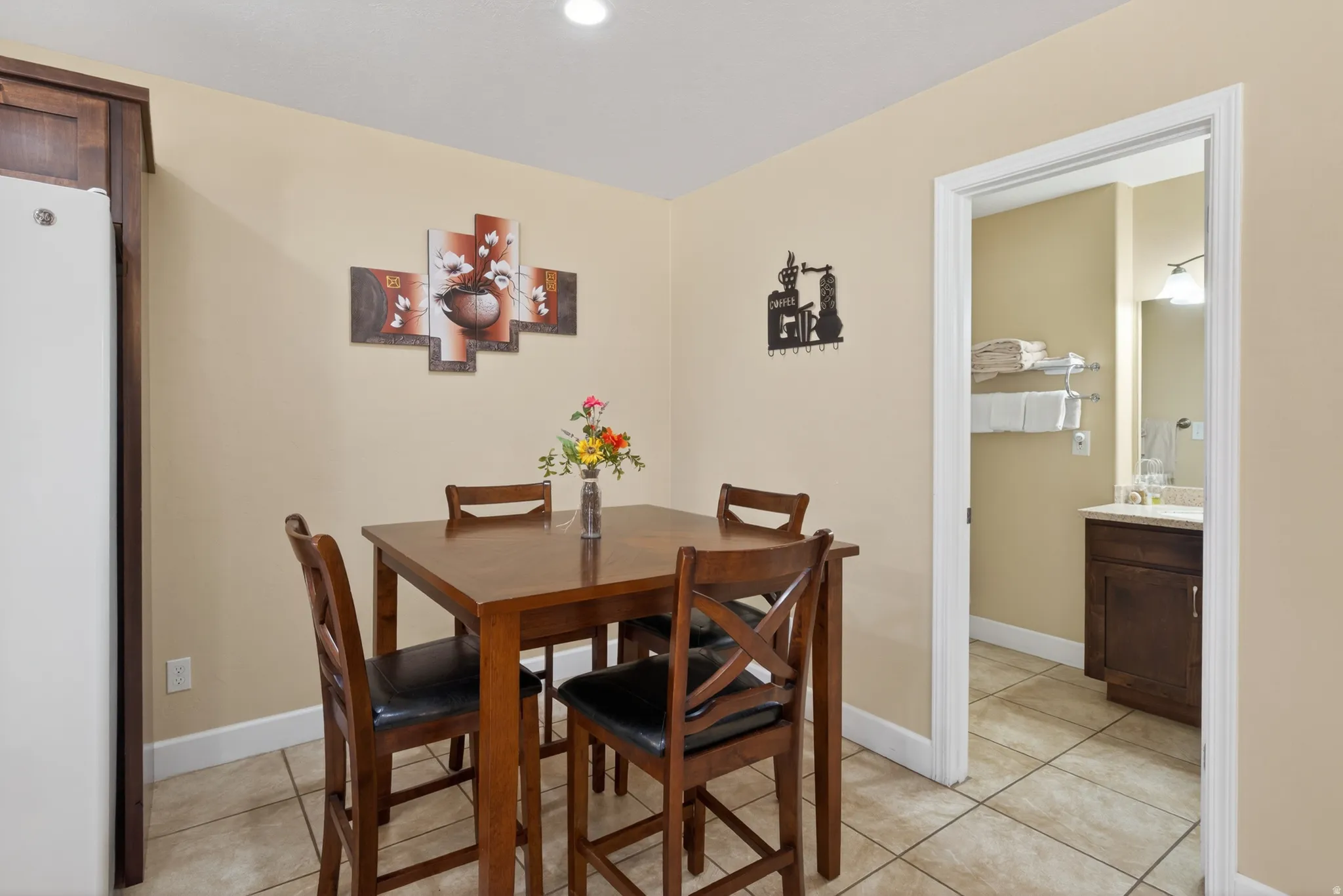 Dining area featuring tile flooring, neutral wall tones, and a doorway to a bathroom with a dark wood-finish vanity and mirror