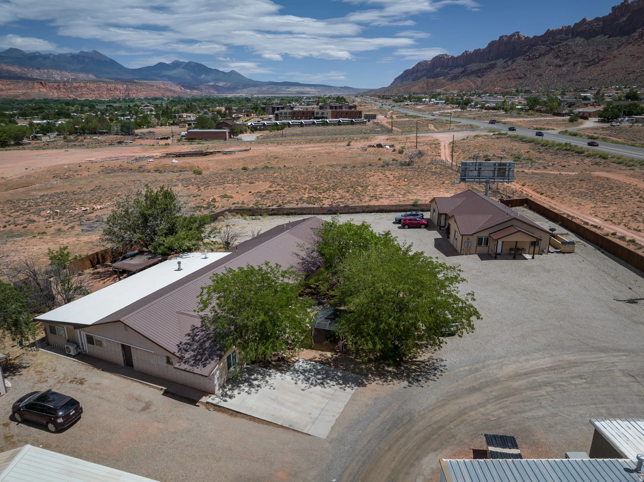 Expansive gravel lot featuring two structures with metal roofs and stucco exteriors