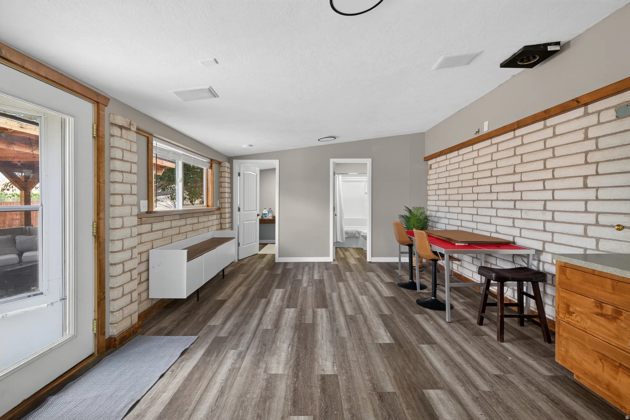 Spacious room featuring wood-finish flooring, a white painted brick accent wall, and recessed lighting