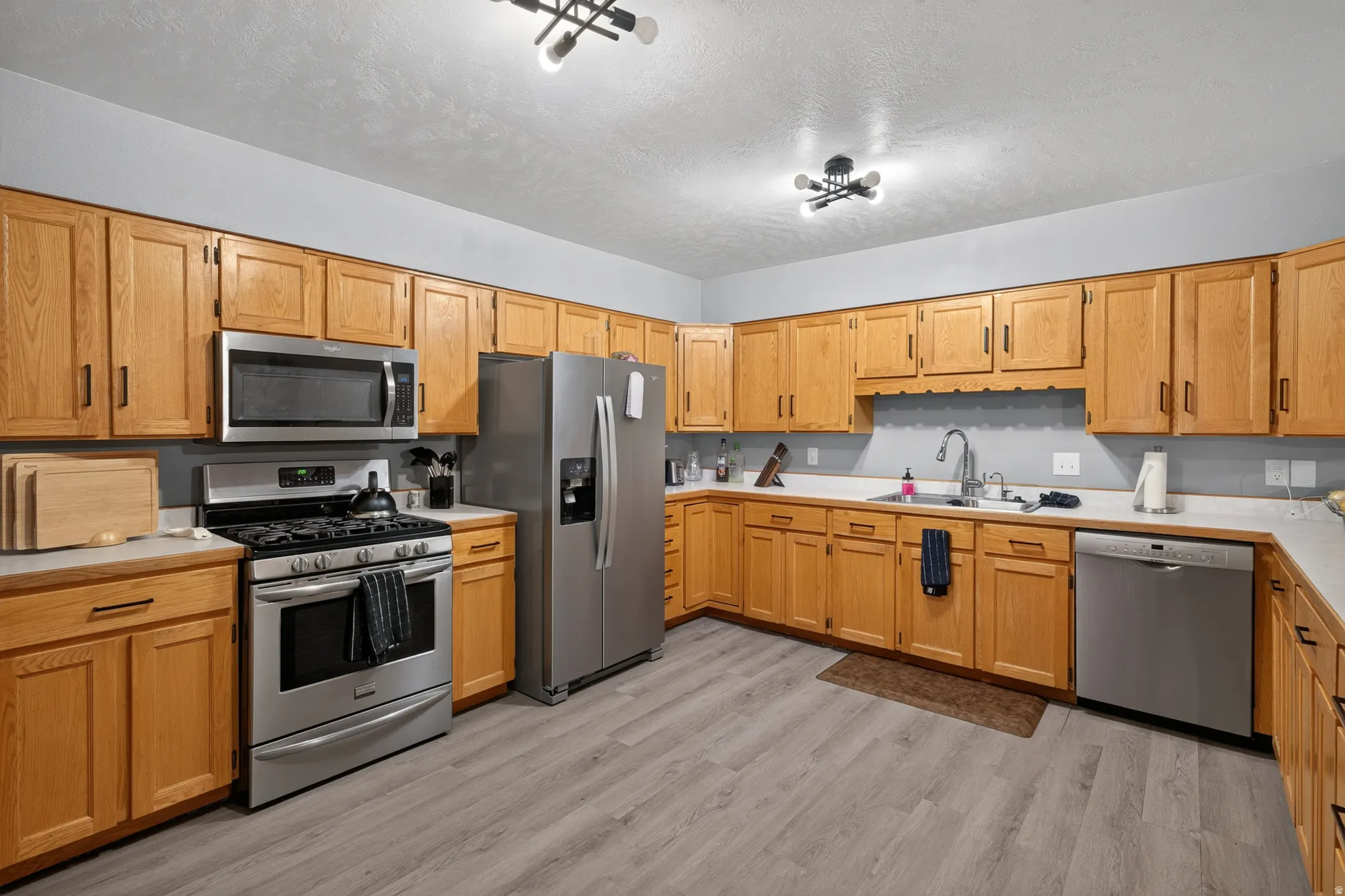 Kitchen featuring abundant wood cabinetry, stainless steel appliances including a gas range, microwave, and dishwasher, light-toned countertops, and wood-finish flooring