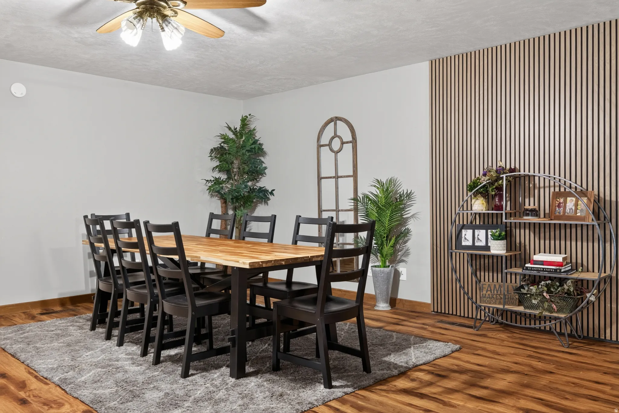Dining area featuring wood-finish flooring, a textured accent wall with vertical slat detailing, and a ceiling fan with integrated lighting