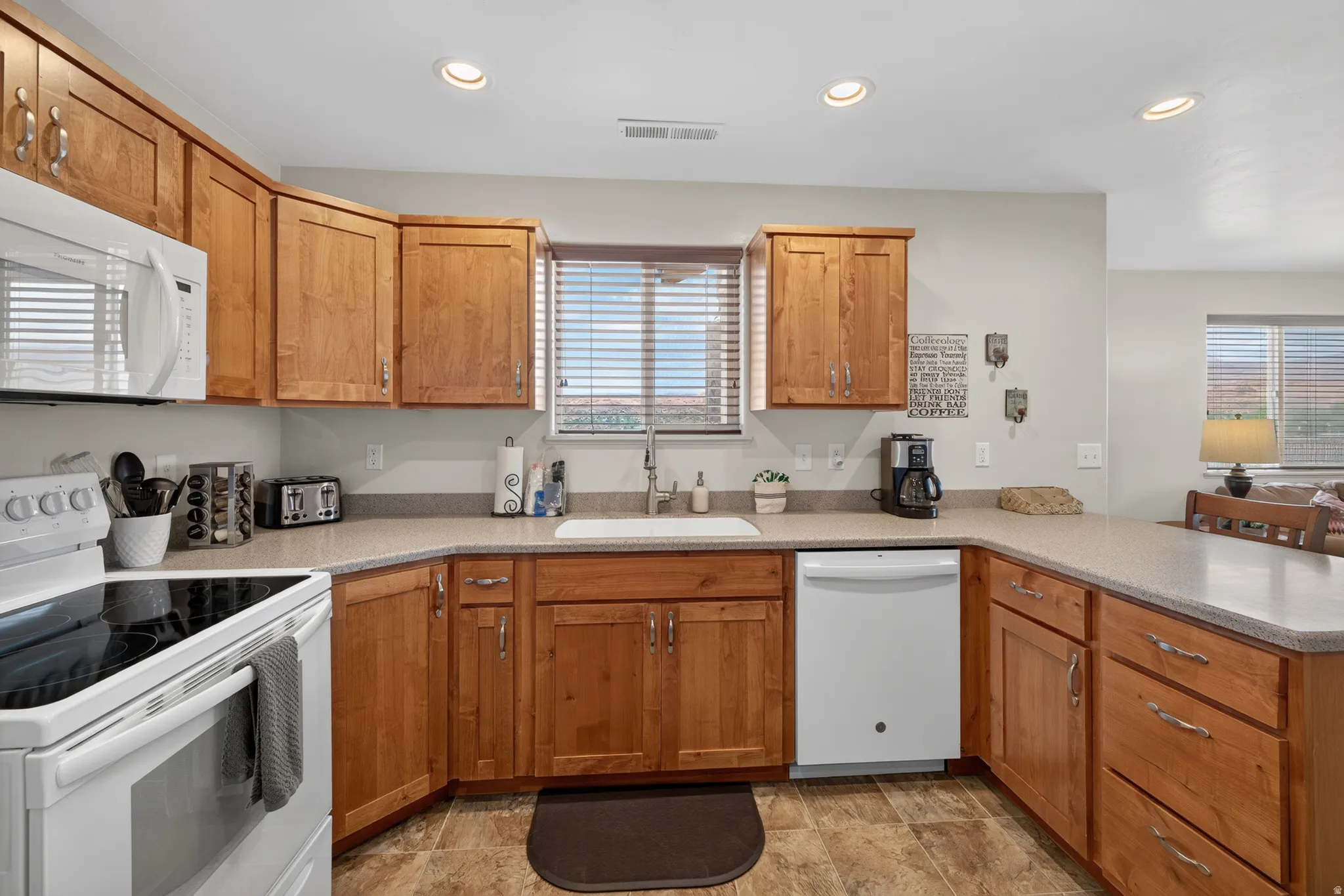 Kitchen featuring wood cabinetry, light-toned countertops, a white built-in dishwasher, white electric range, and a white over-the-range microwave