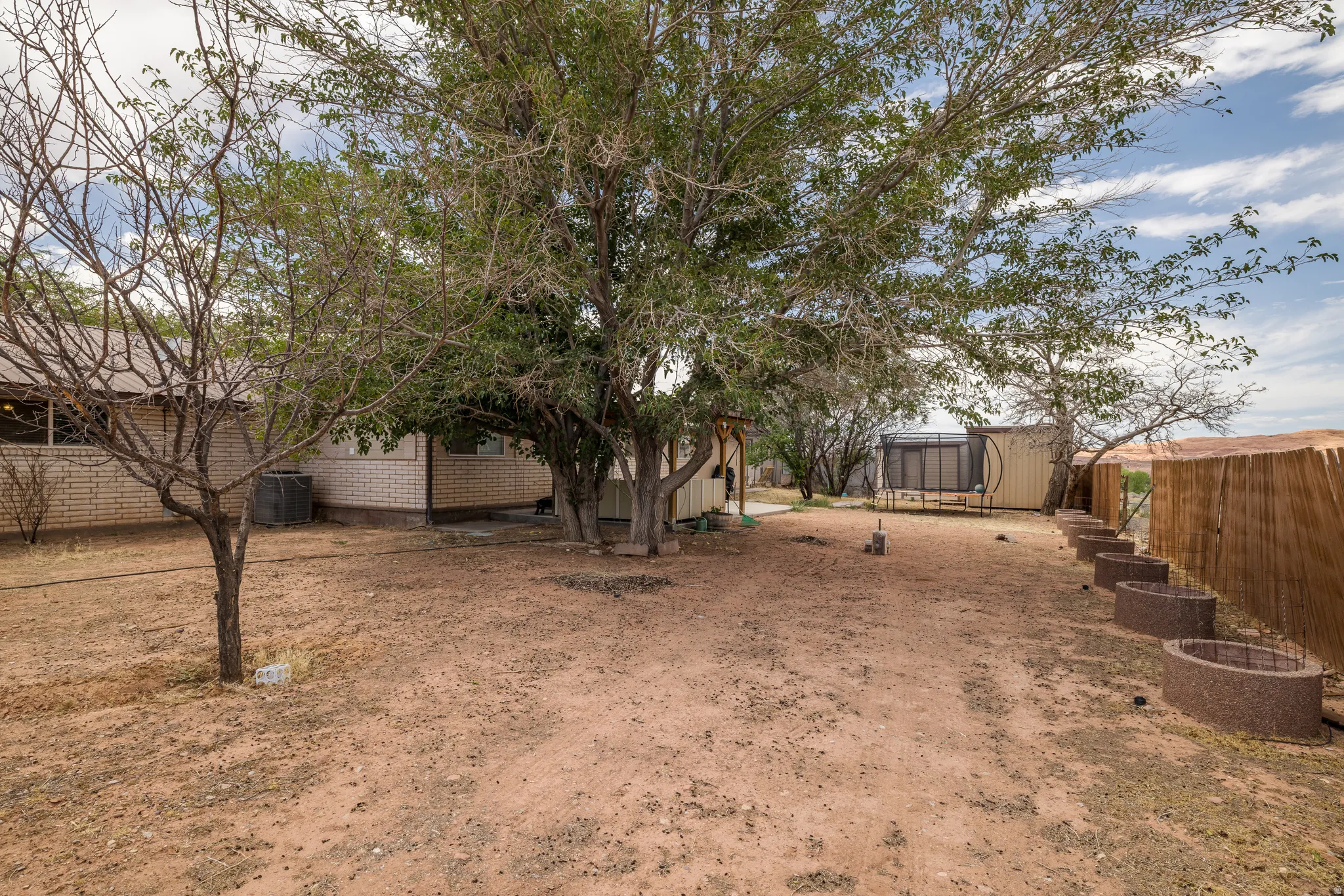 Expansive yard featuring mature trees, a wooden privacy fence, and a series of built-in circular planters