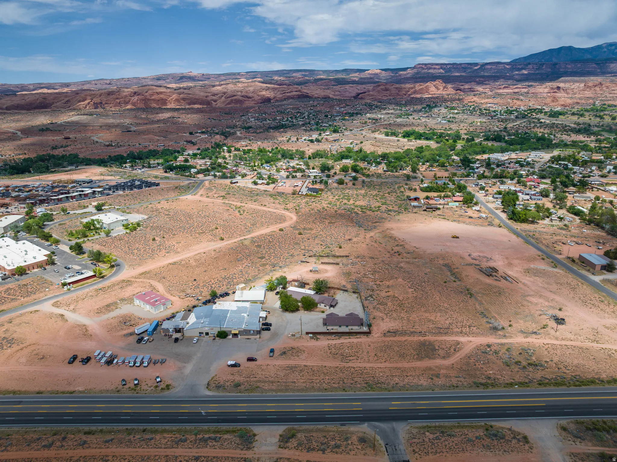 Expansive arid landscape featuring scattered buildings, a prominent multi-lane roadway, and distant mountain formations