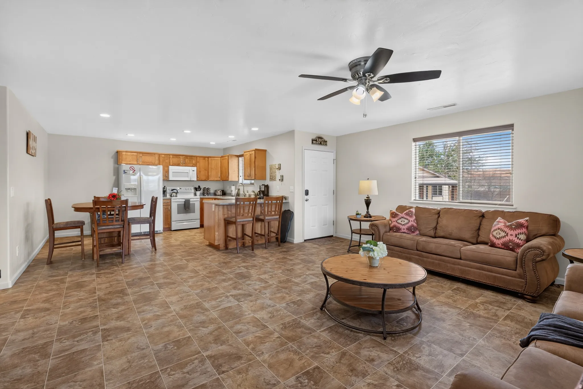 Open-concept living area featuring tile flooring, a kitchen with wood cabinetry and white appliances, a dining area, and a ceiling fan