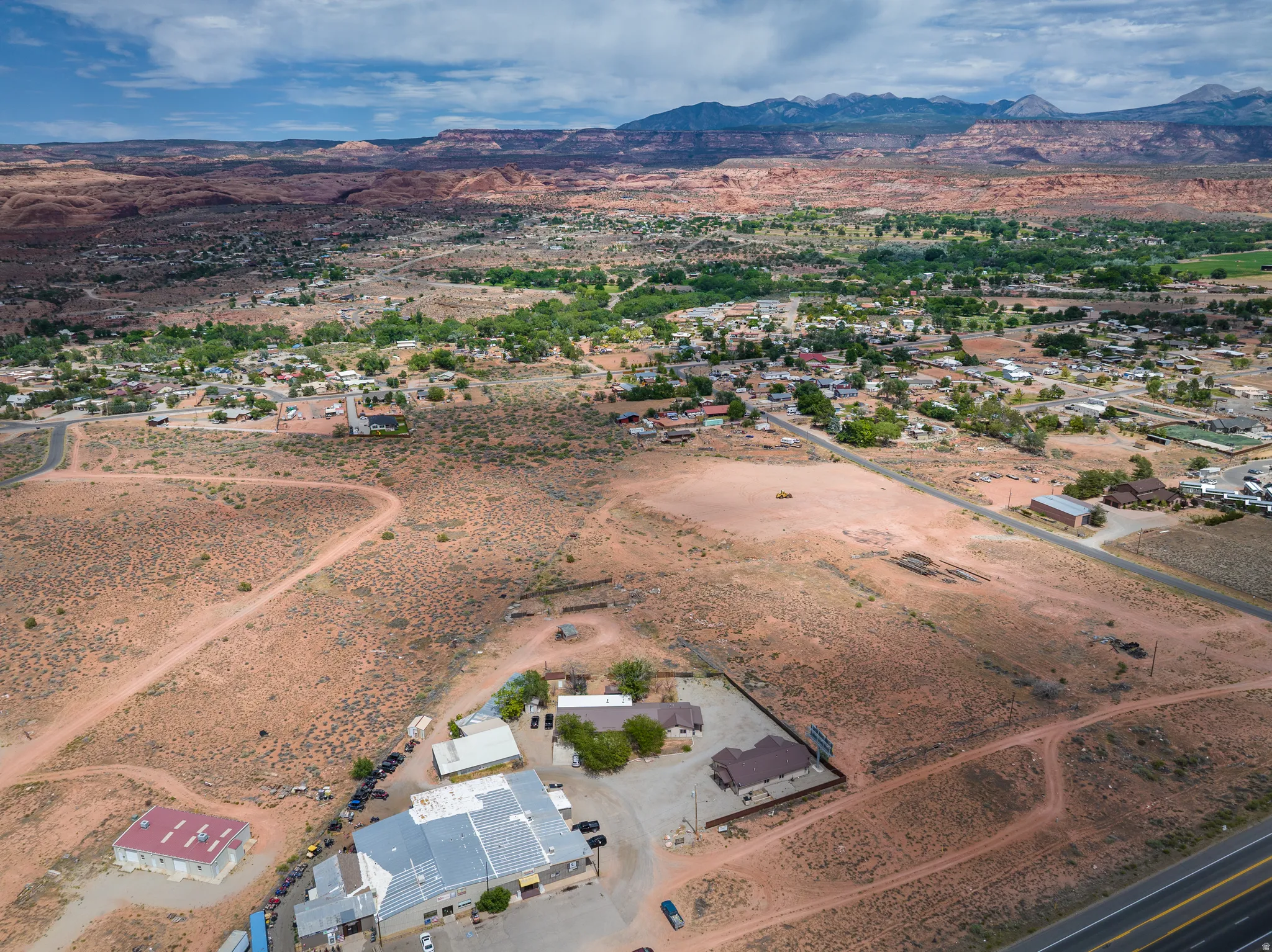 Expansive desert landscape featuring multiple structures, paved roads, and distant mountain ranges