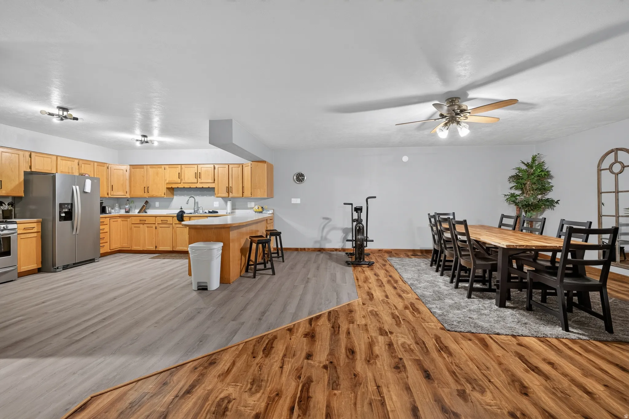 Open-concept kitchen and dining area featuring light wood cabinetry, a curved breakfast bar, stainless steel appliances, and contrasting wood-finish flooring