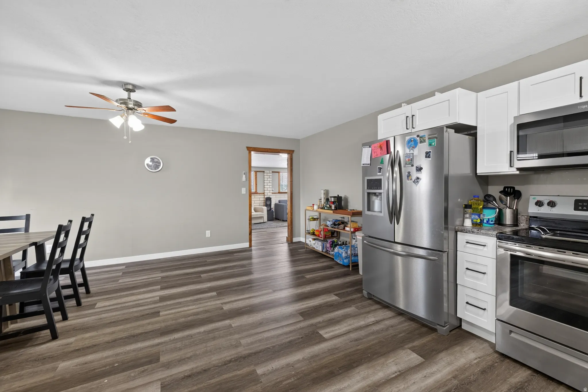 Kitchen and dining area featuring wood-finish flooring, white cabinetry, stainless steel appliances, and a ceiling fan with integrated lighting
