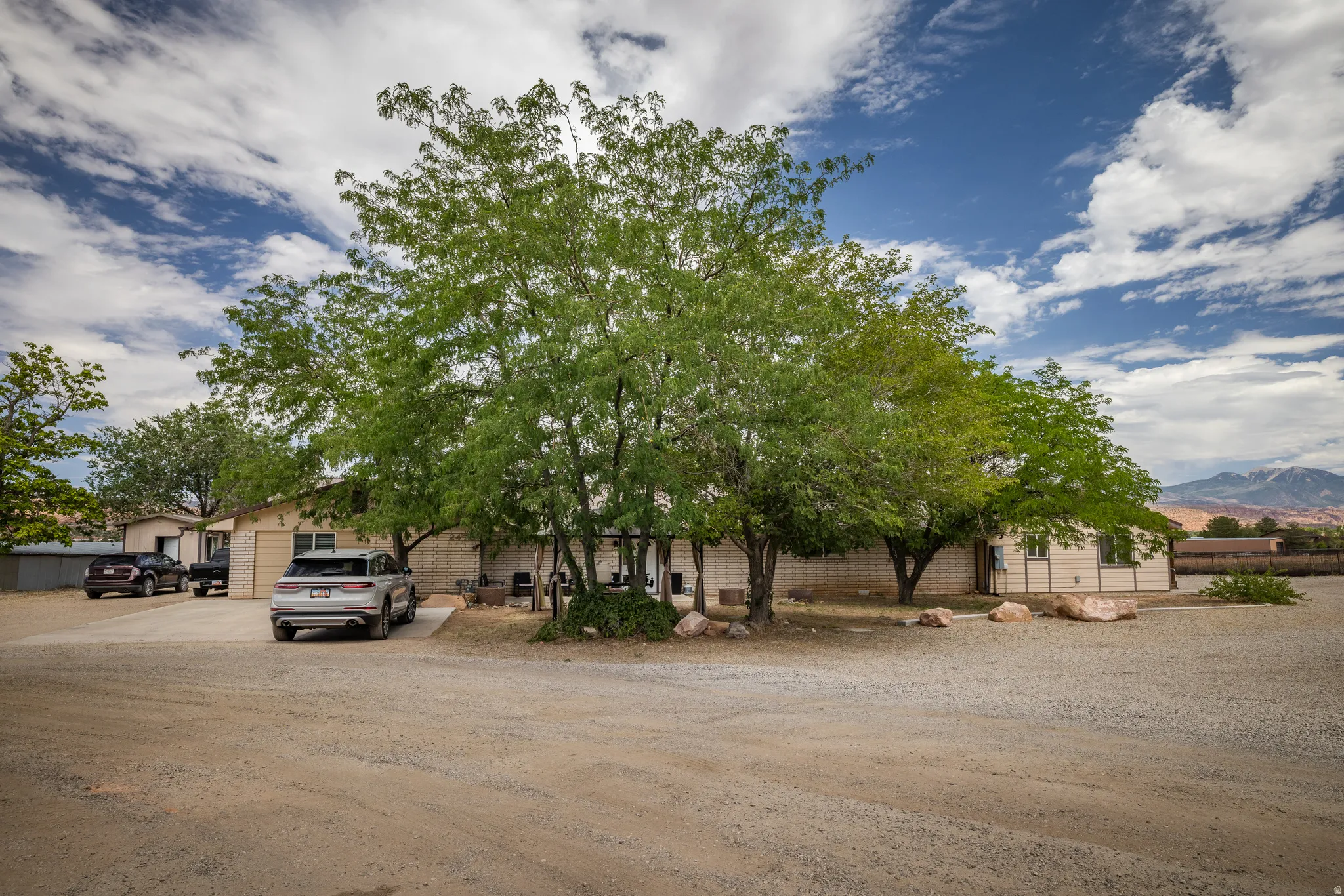 Expansive gravel lot with mature trees providing partial shade