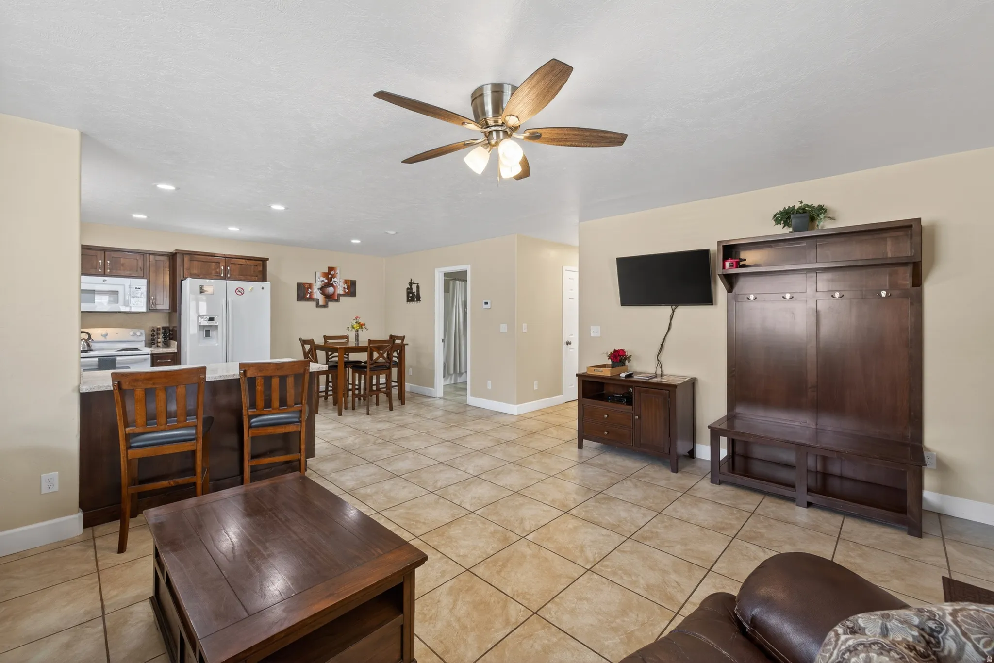 Open-concept living space featuring ceramic tile flooring, a kitchen with wood cabinetry and white appliances, and a dining area with a wood-finish table