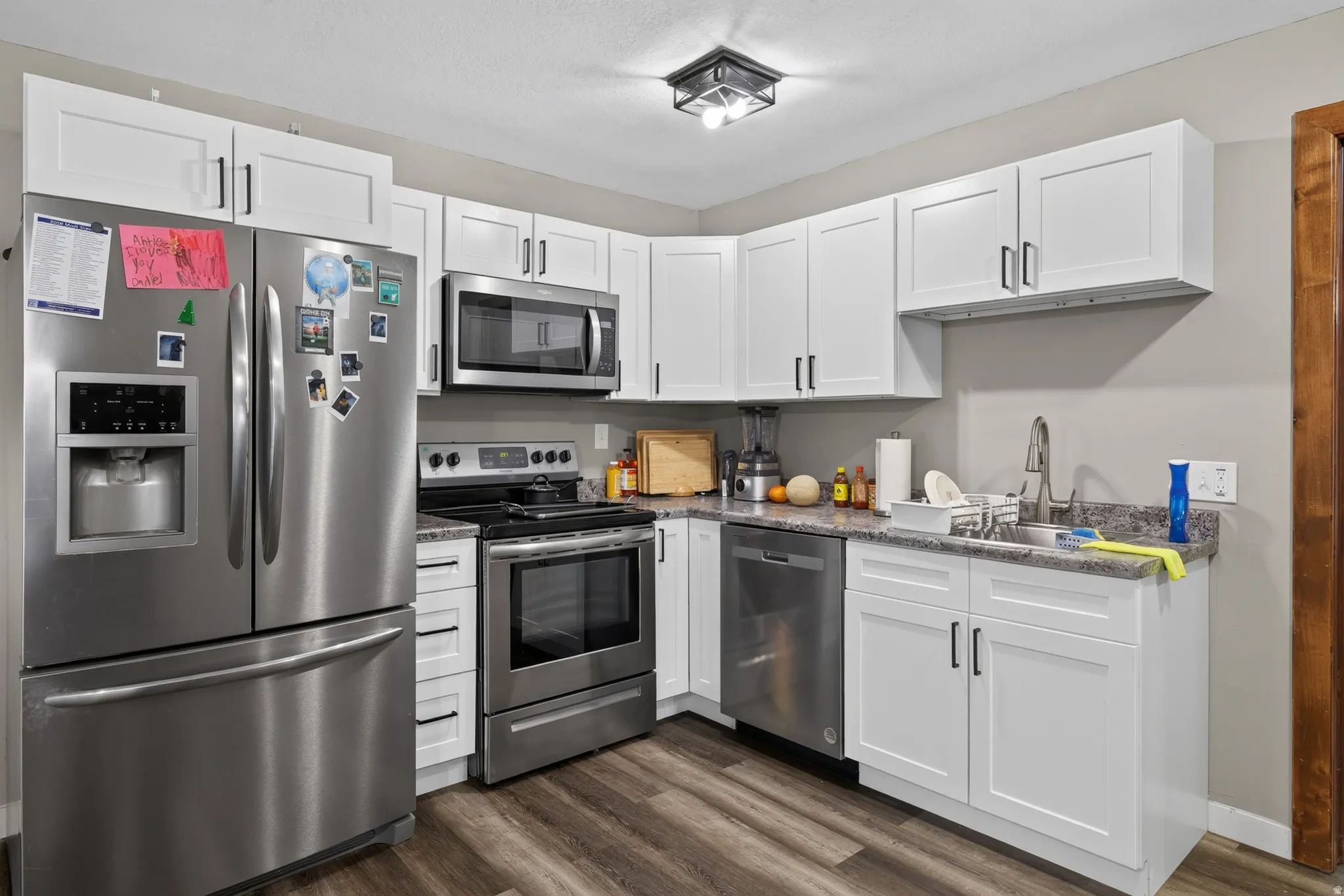 Kitchen featuring white shaker-style cabinetry, stainless steel appliances, granite-look countertops, and wood-finish flooring