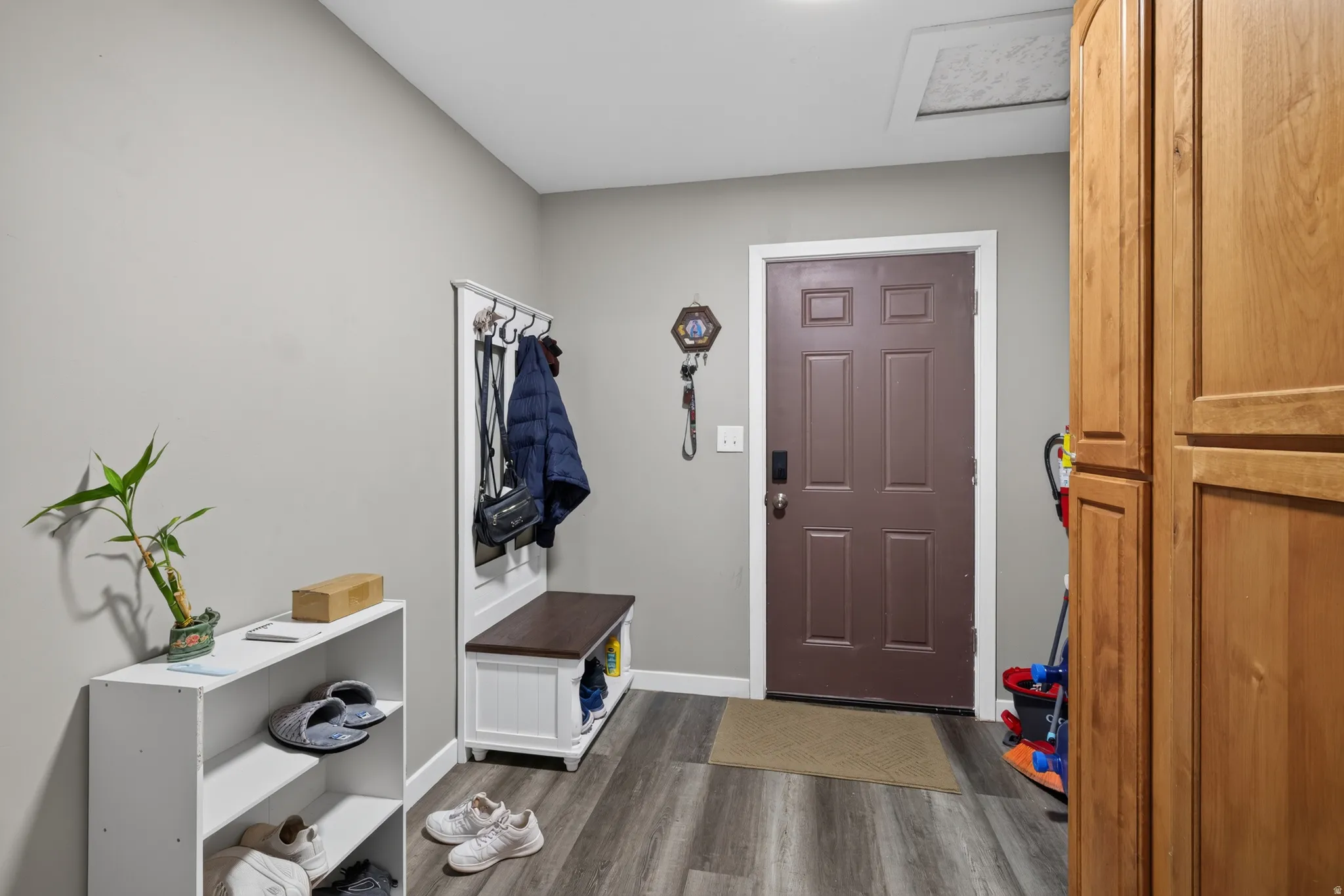 Entryway featuring wood-finish flooring, a paneled door with white trim, light gray walls, and built-in wood cabinetry