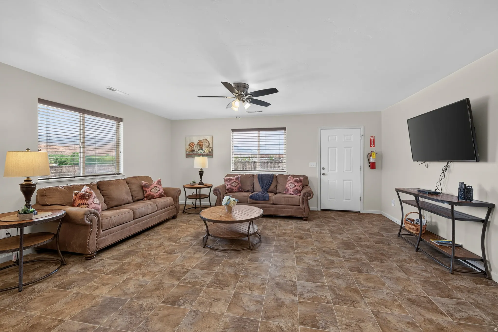 Spacious living area featuring multi-toned tile flooring, neutral wall paint, and multiple windows with horizontal blinds