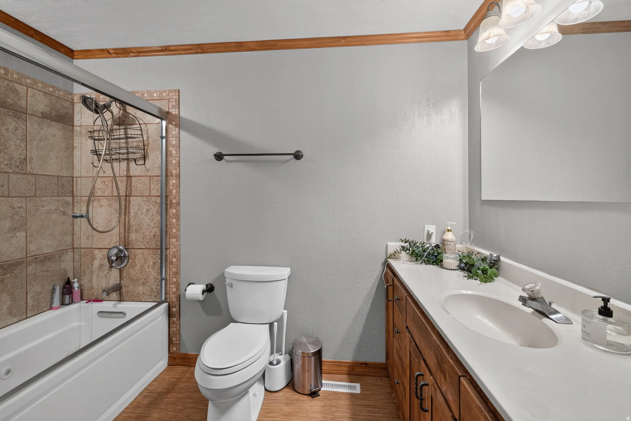Bathroom featuring a white bathtub, glass shower enclosure with tile surround, wood-finish flooring, a white vanity countertop with an integrated sink, and wood cabinetry