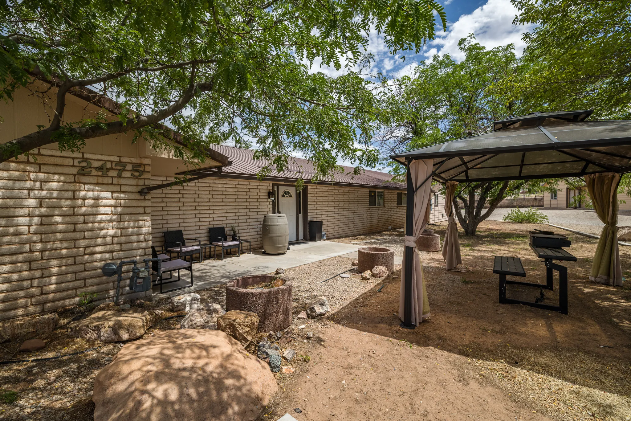Outdoor living area featuring a permanent gazebo with curtains, two fire pits, a built-in outdoor cooking station, and mature shade trees