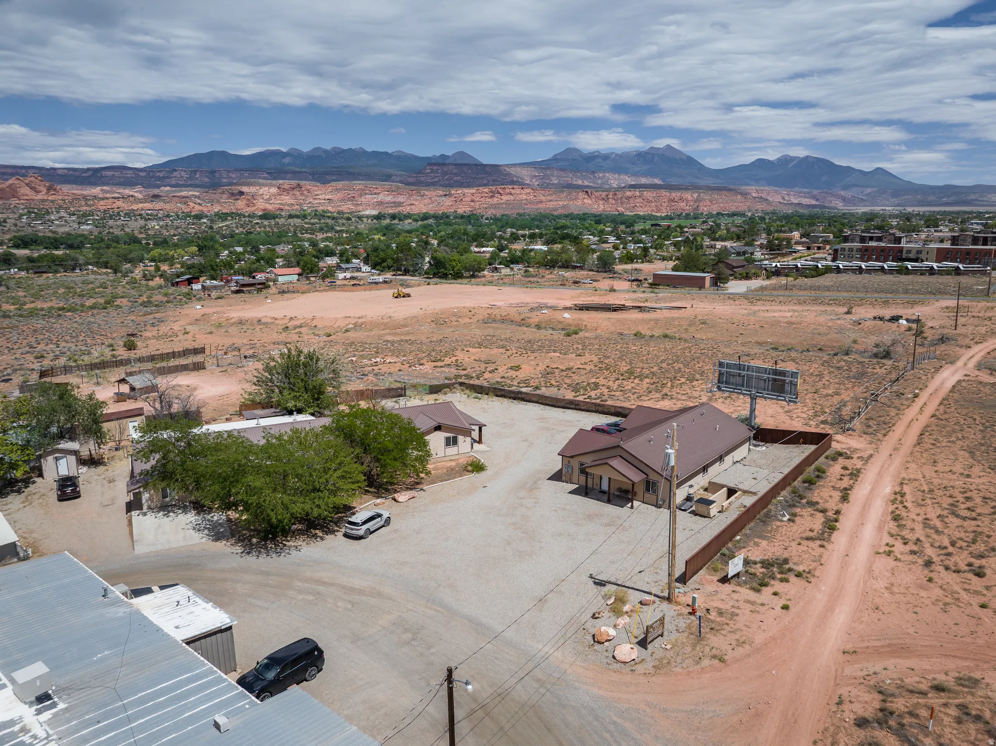 Aerial perspective showcasing a commercial property with a brown metal roof building, featuring a paved parking area and perimeter fencing