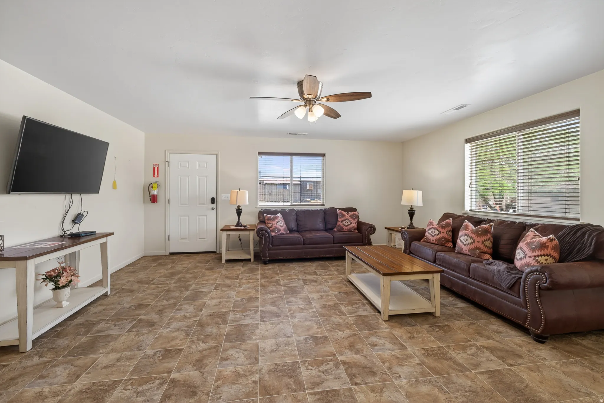 Spacious living area featuring neutral wall tones, tile flooring, and a ceiling fan