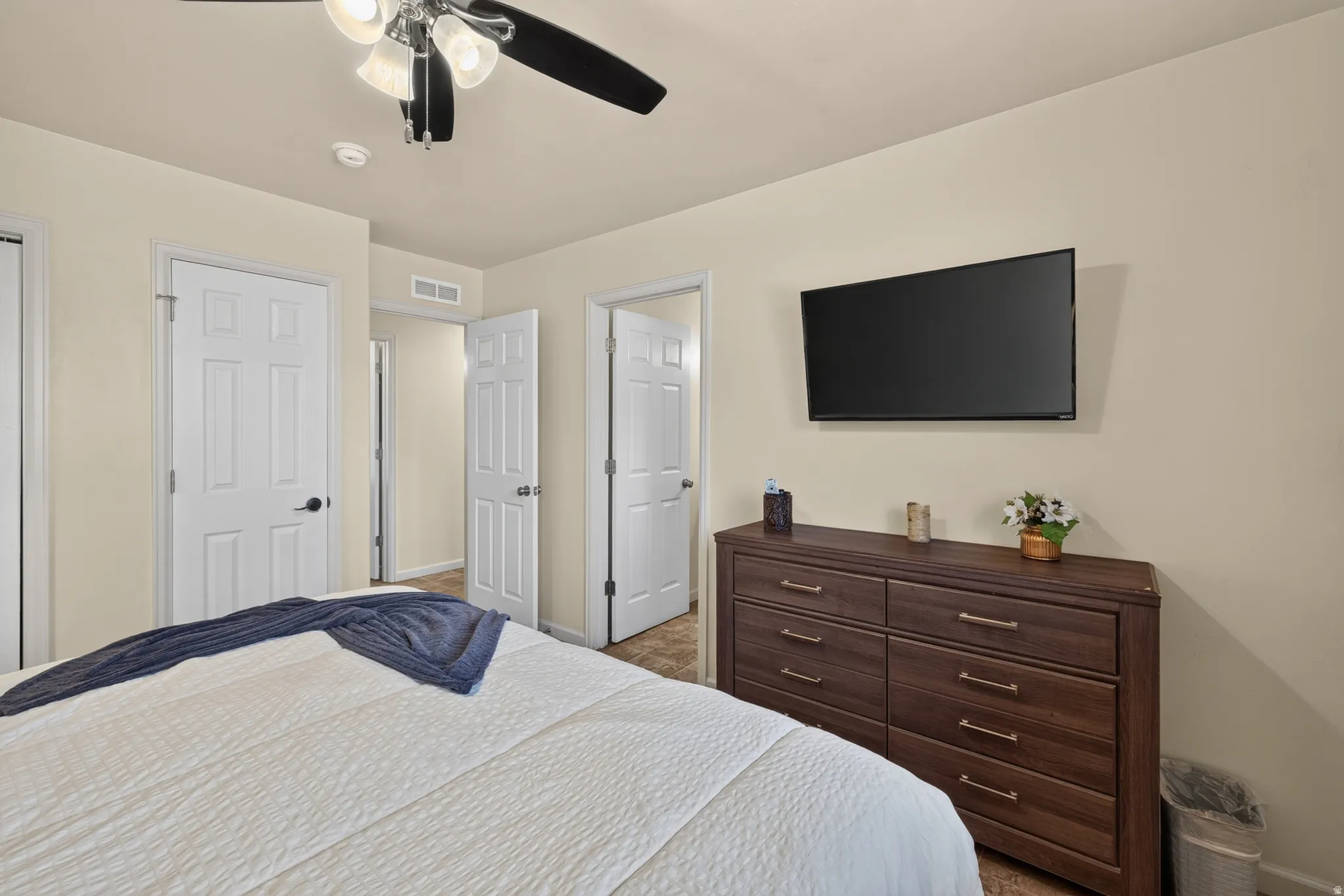 Bedroom featuring neutral-toned walls, a ceiling fan with integrated lighting, and multiple paneled doors with black hardware
