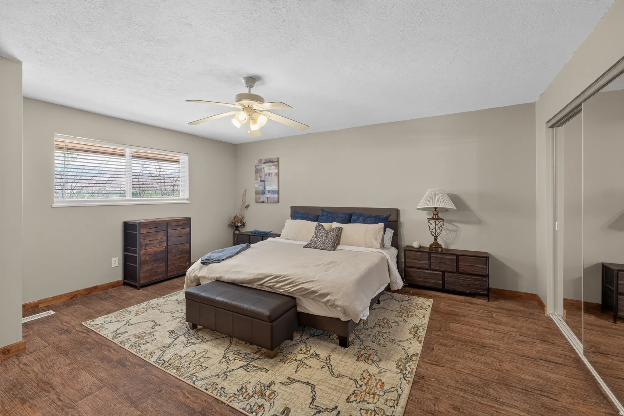 Spacious room featuring wood-finish flooring, a ceiling fan, and a large window with blinds