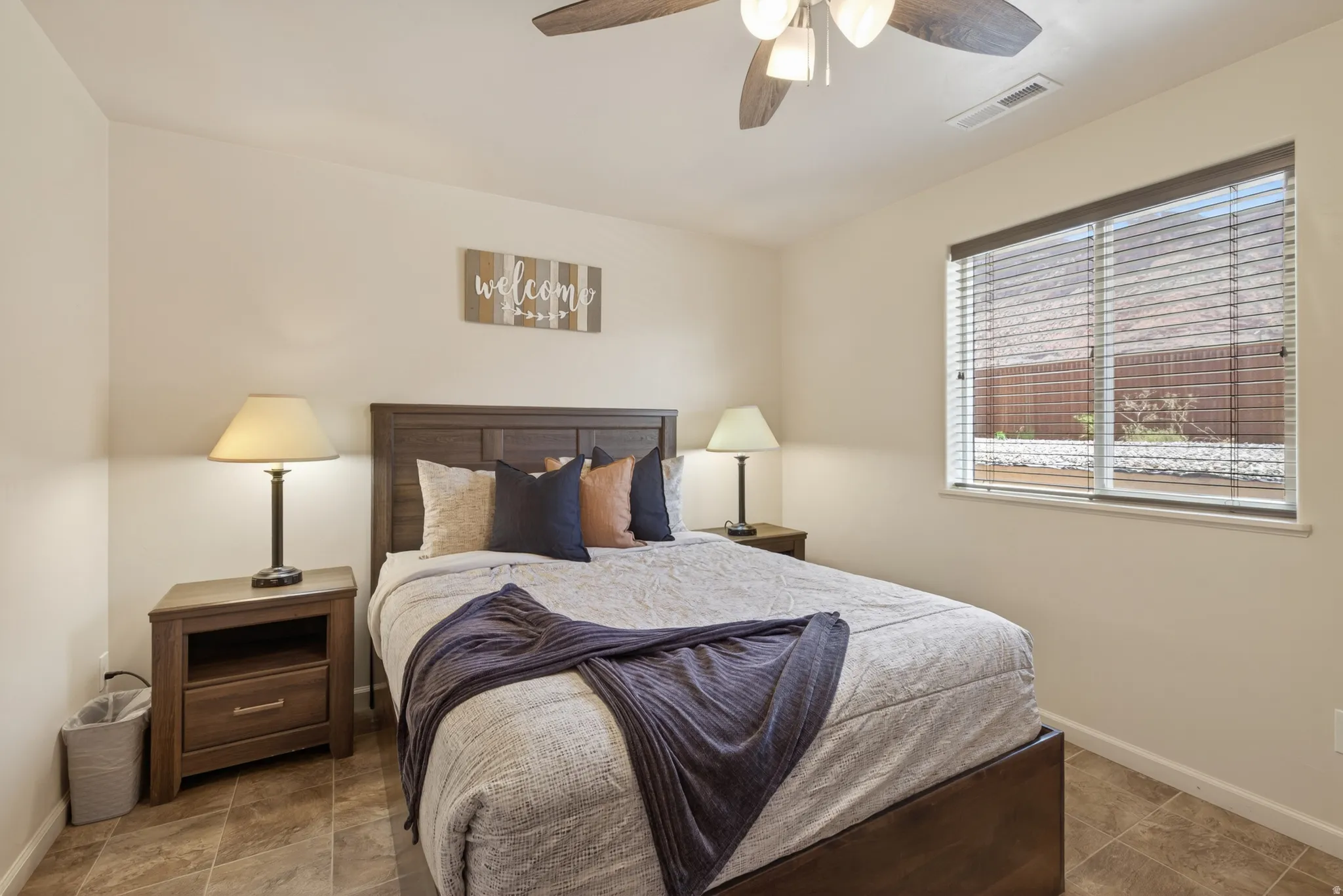 Bedroom featuring tile flooring, a window with horizontal blinds, a ceiling fan with integrated lighting, and a paneled wood headboard