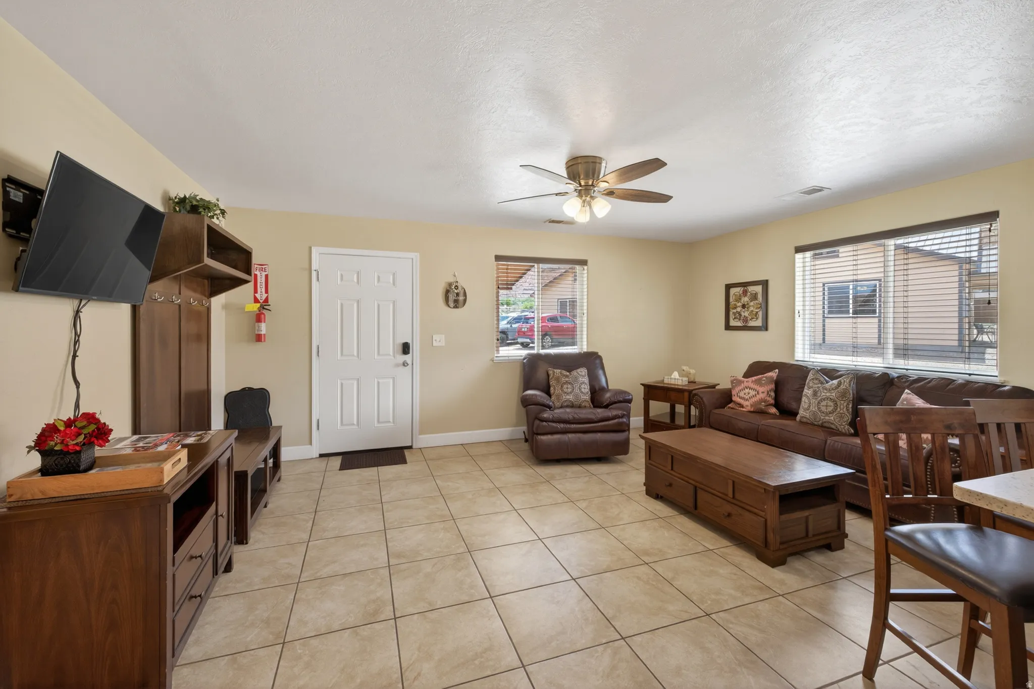 Spacious living area featuring tile flooring, a ceiling fan, and multiple windows with horizontal blinds