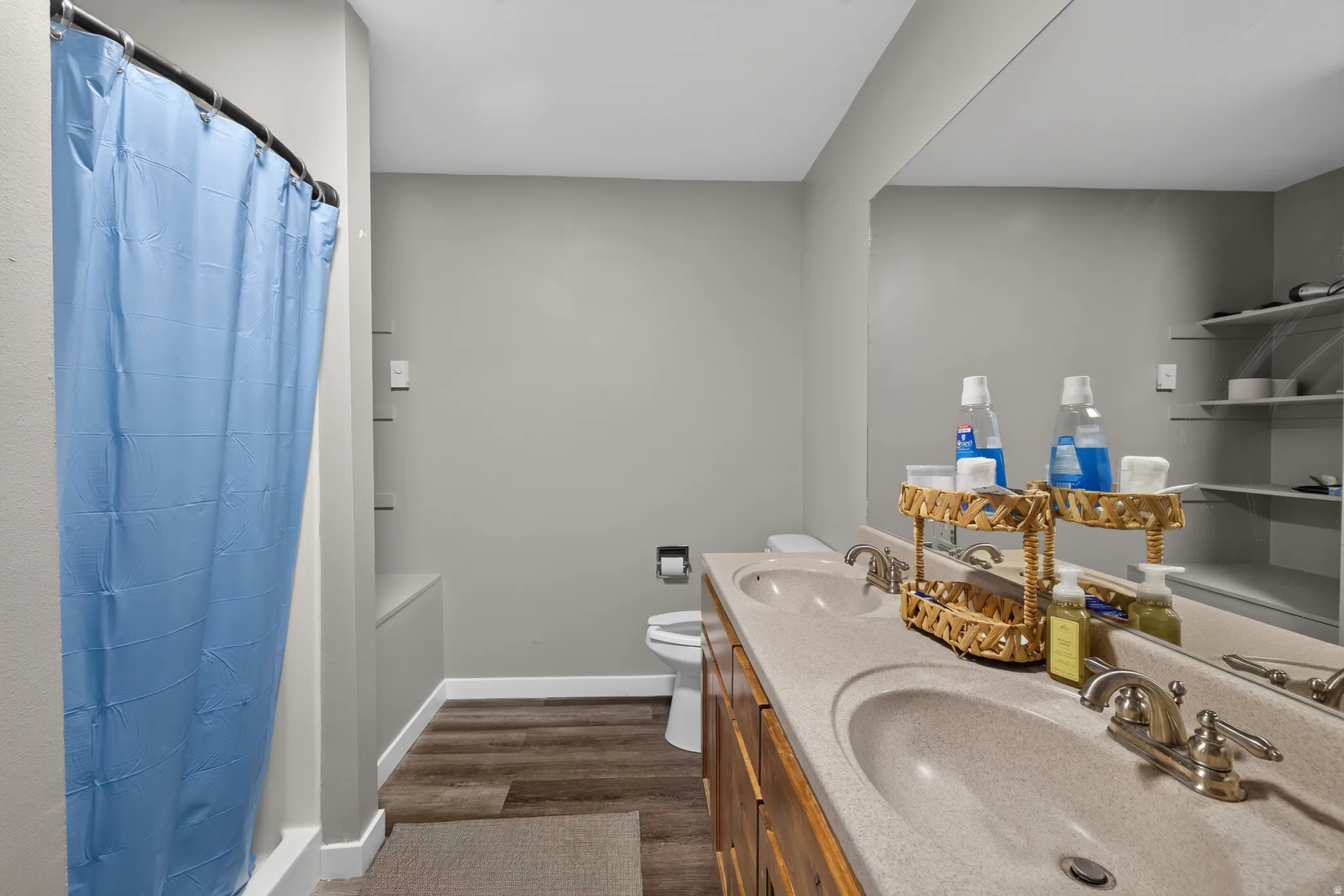 Bathroom featuring a double vanity with integrated sinks, wood-finish flooring, a wall-mounted mirror, and built-in shelving