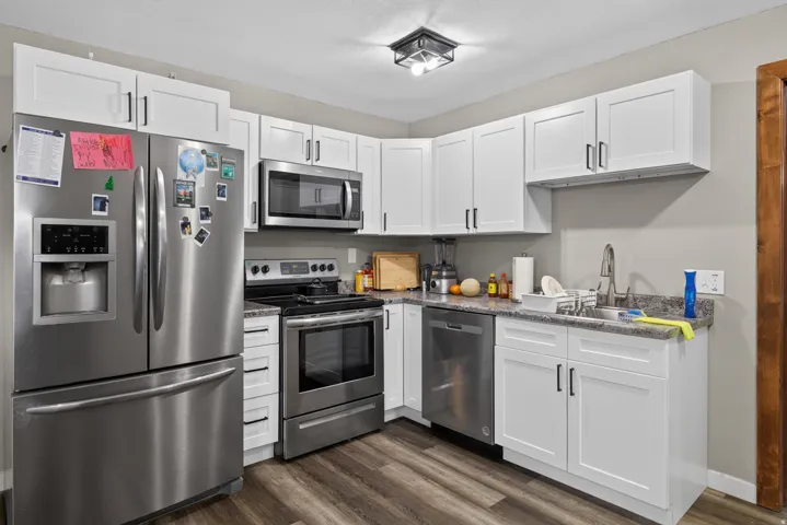 Kitchen featuring white shaker-style cabinetry, stainless steel appliances, granite-look countertops, and wood-finish flooring