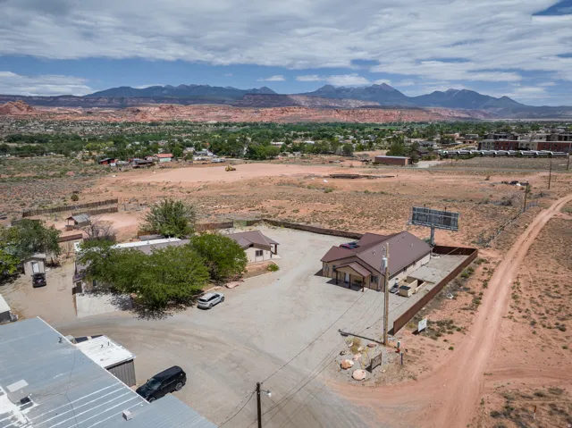 Aerial perspective showcasing a commercial property with a brown metal roof building, featuring a paved parking area and perimeter fencing